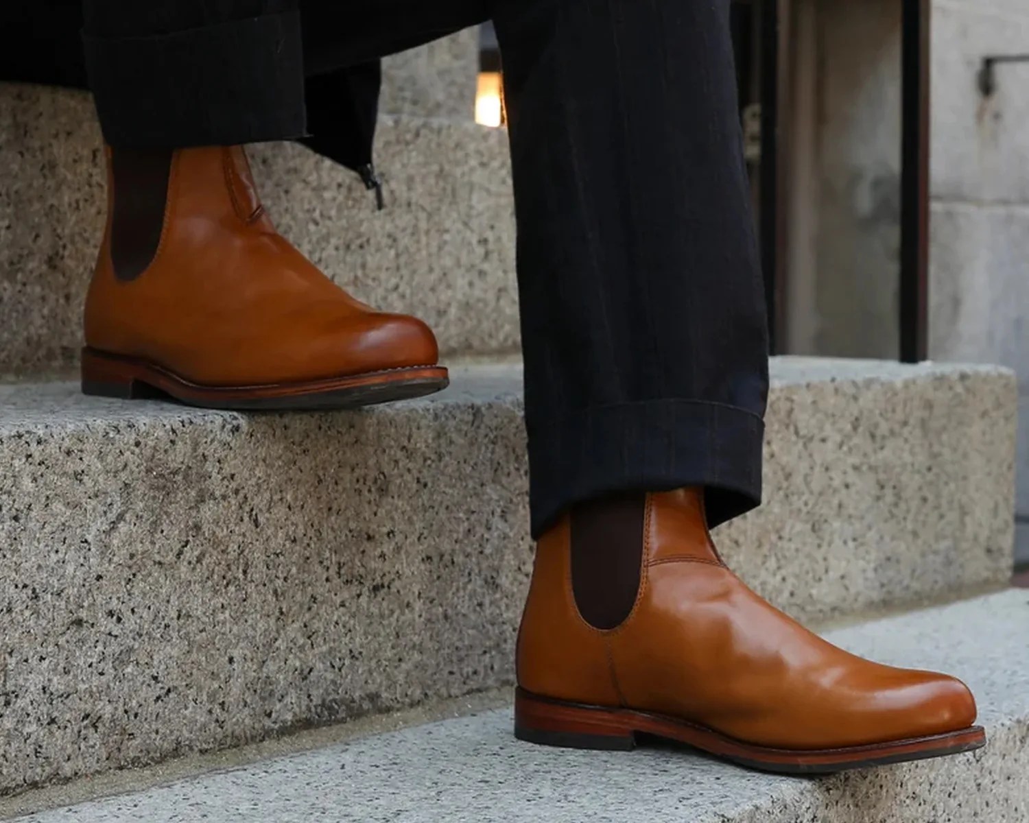 Pair of tan leather Chelsea boots worn with black pants on stone steps.