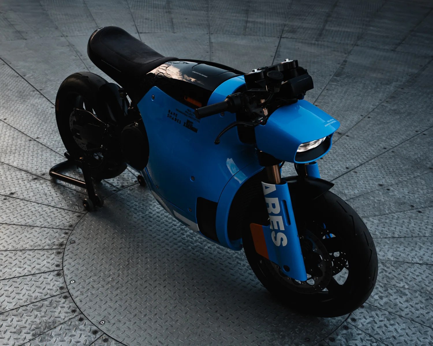 Blue and black modern motorcycle with "ARES" text on the front fork, parked on a metal circular platform.