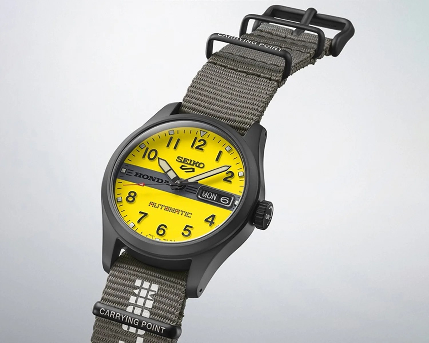 Black Seiko wristwatch with bright yellow dial, gray fabric strap, and day-date display showing Monday the 6th.