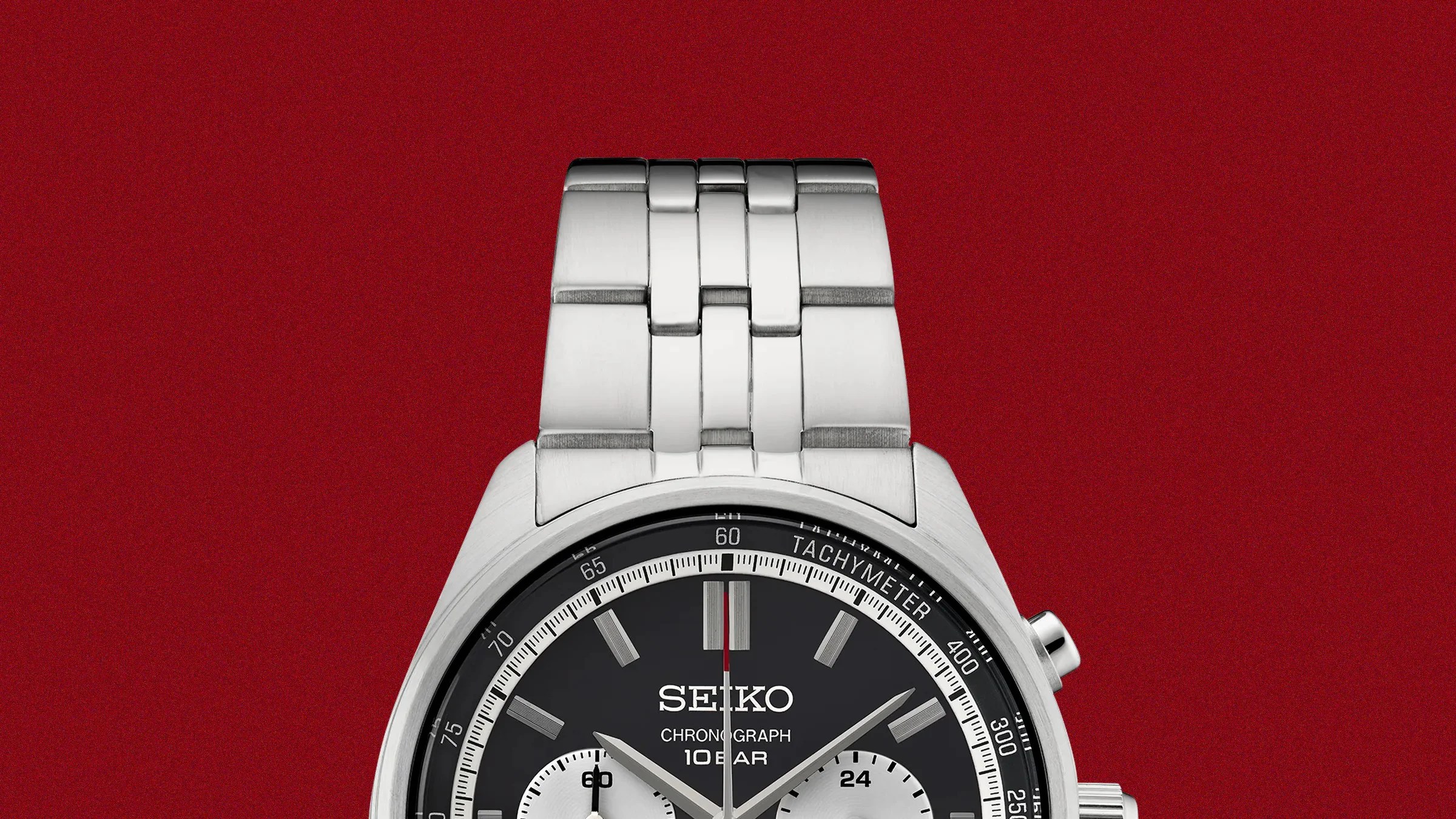 Silver metal link watch band attached to a Seiko chronograph watch with a black dial on a red background.