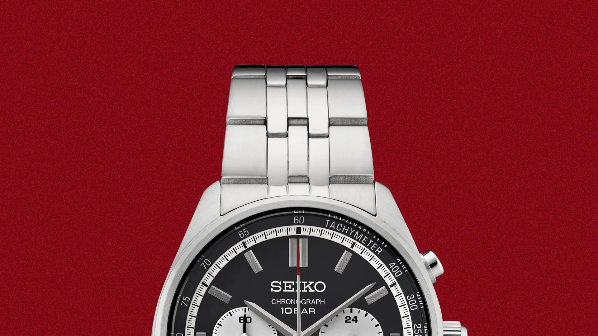 Silver metal link watch band attached to a Seiko chronograph watch with a black dial on a red background.