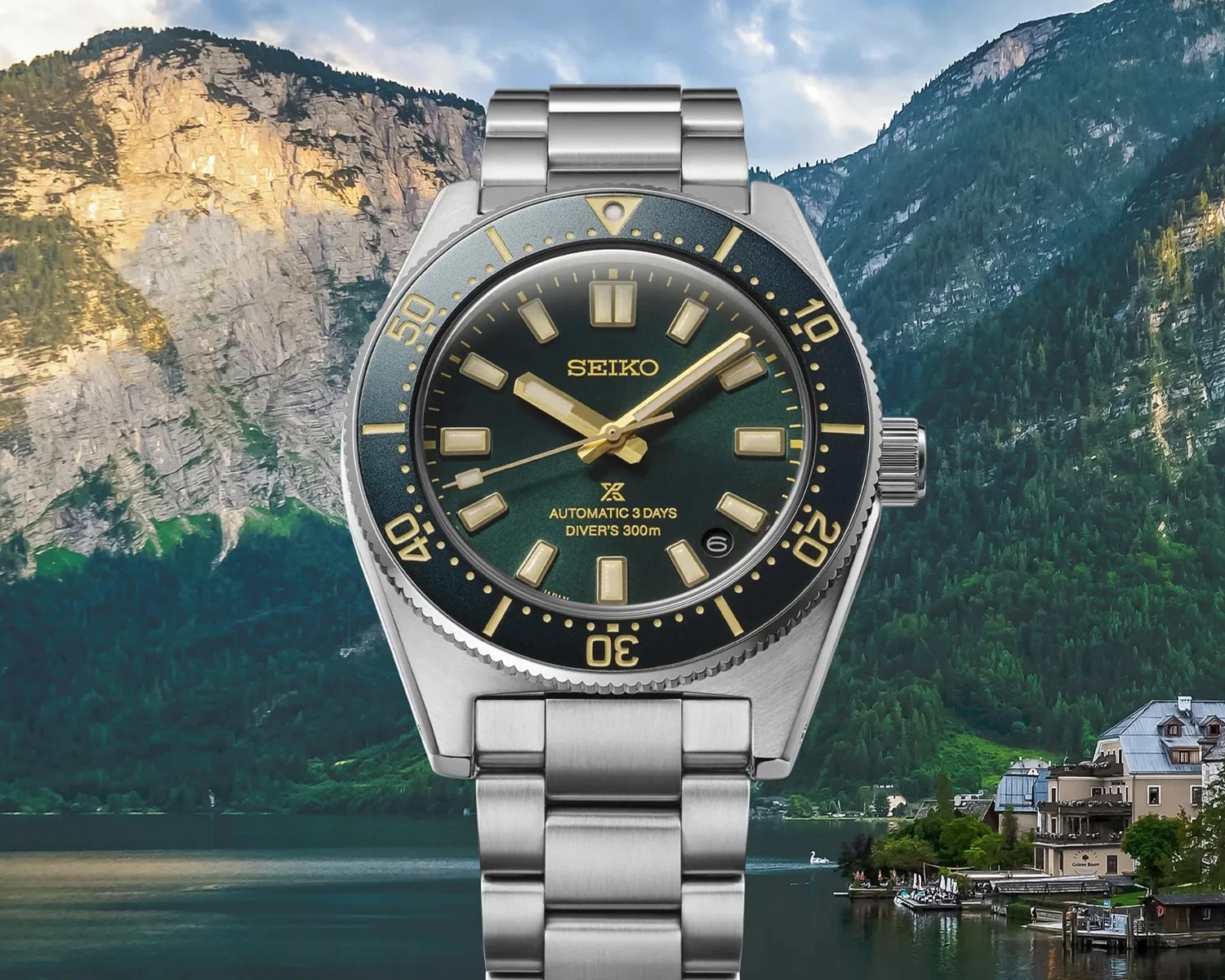 Silver Seiko diver's watch with green dial, gold accents, and stainless steel bracelet against mountain lake background.