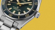 Close-up of a Seiko diver's watch with a green dial, gold-tone markers, and a stainless steel bracelet on a yellow background.
