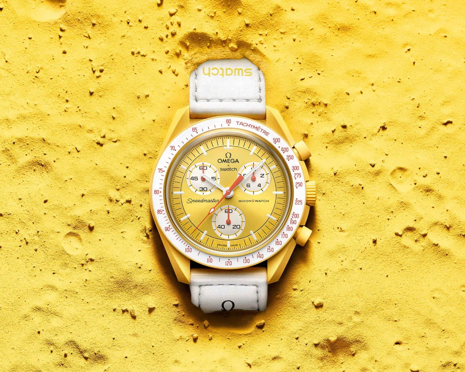 Yellow Omega x Swatch Speedmaster MoonSwatch with white tachymeter bezel and white fabric strap on yellow textured surface.