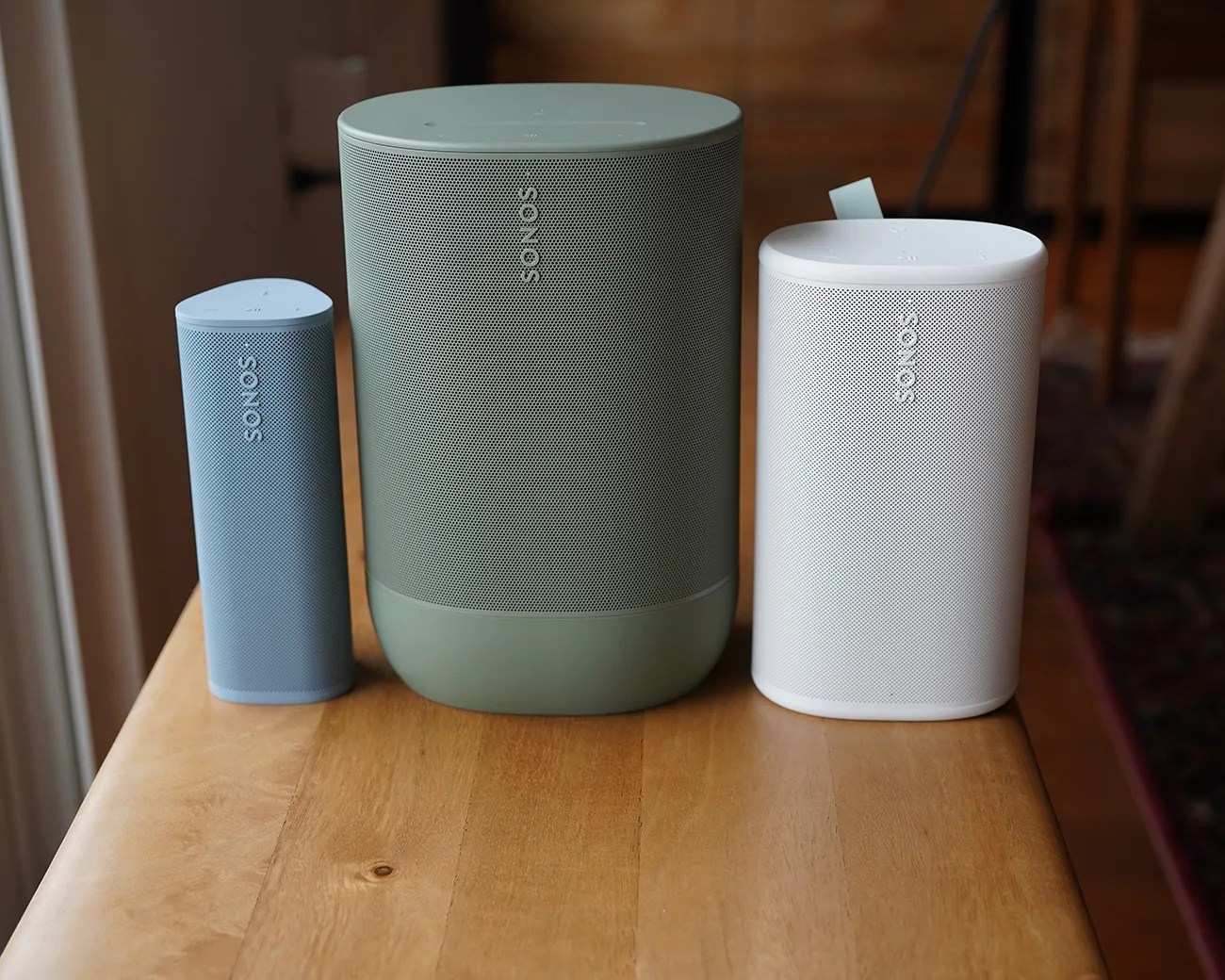Three Sonos wireless speakers in blue, green, and white on a wooden table.