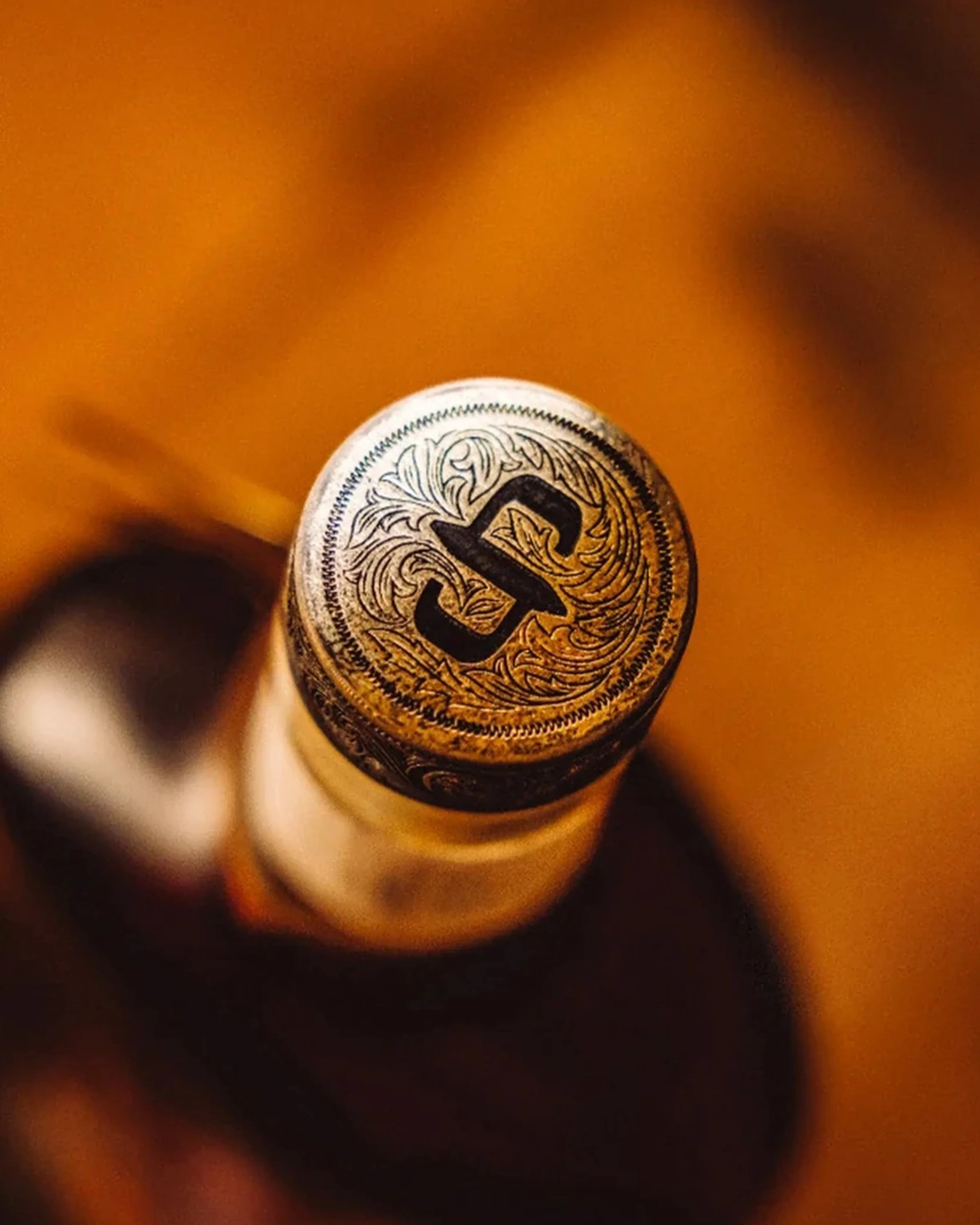 Close-up of a bottle cap with intricate floral engravings and a bold letter "S" on top.