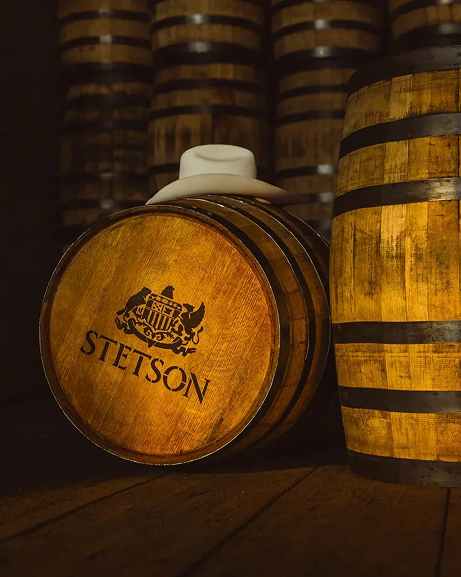 White cowboy hat resting on a wooden barrel with "STETSON" logo in a dimly lit storage room.