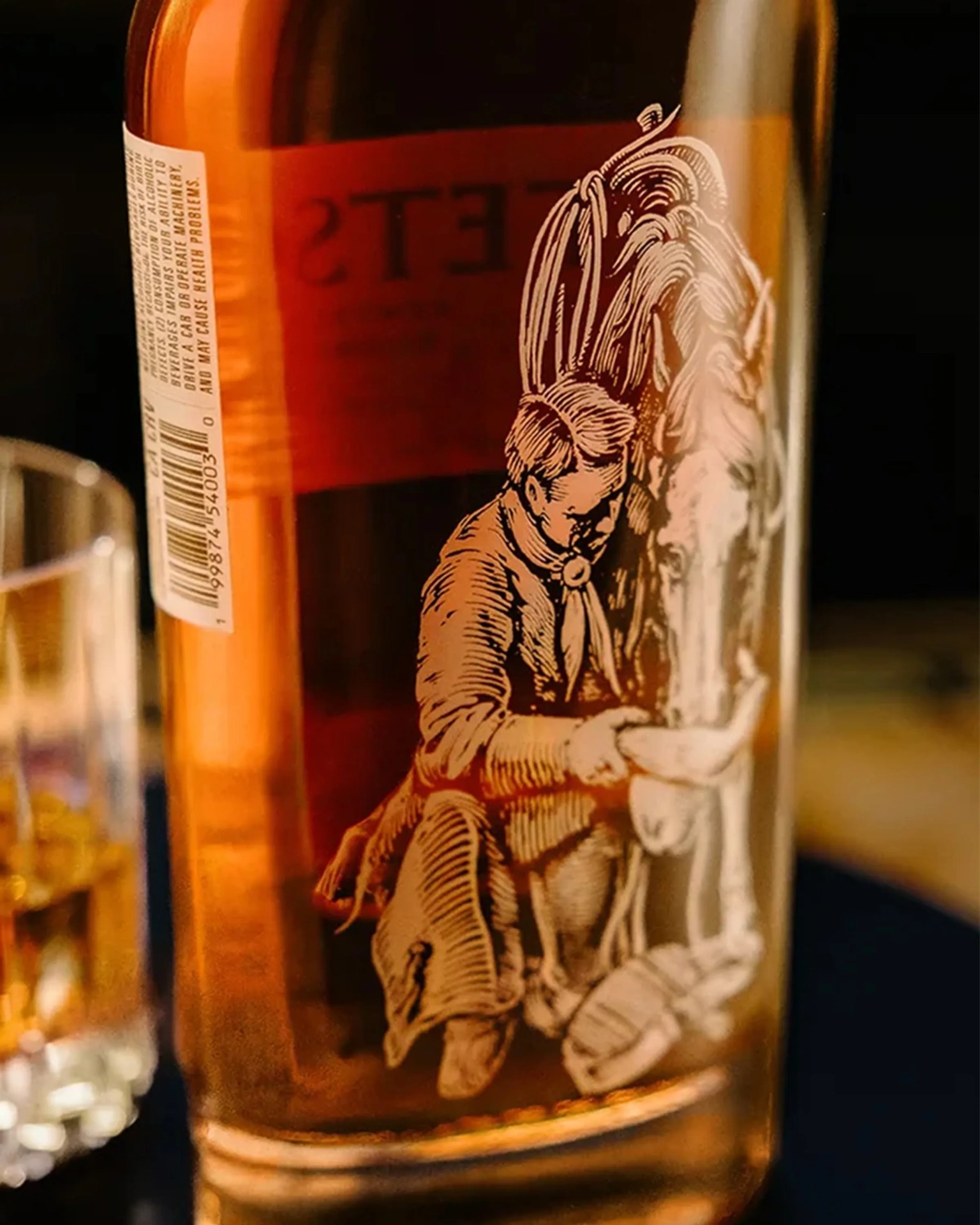 Close-up of a whiskey bottle with an etched illustration of a man feeding a horse.