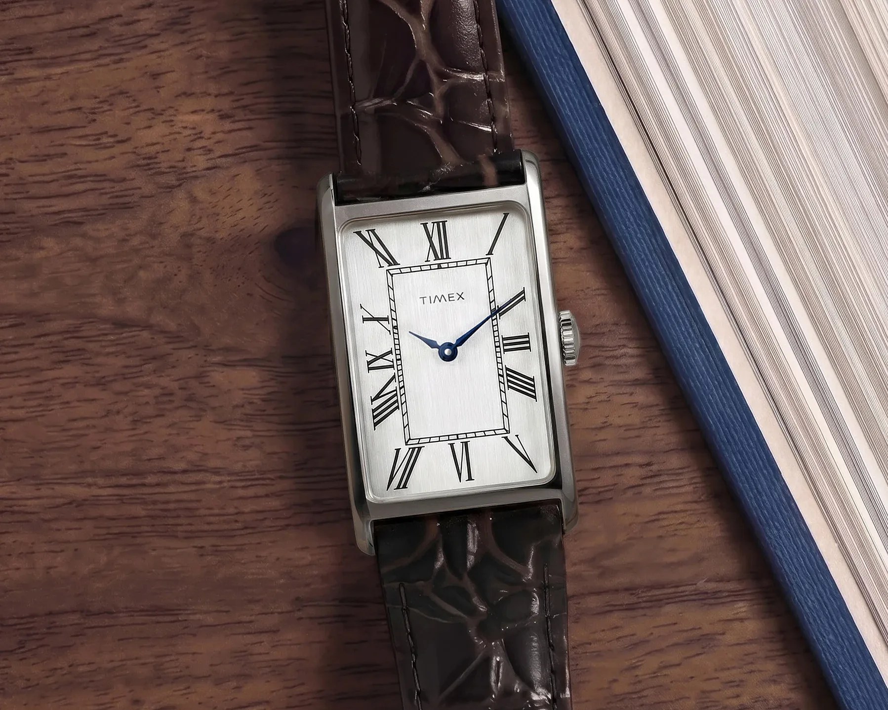 Rectangular silver Timex watch with Roman numerals and dark brown crocodile leather strap on a wooden surface.