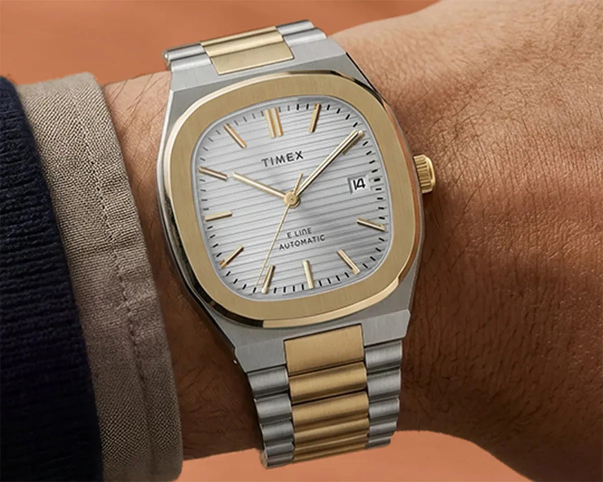 Two-tone silver and gold Timex wristwatch with a white textured dial and date display worn on a wrist.