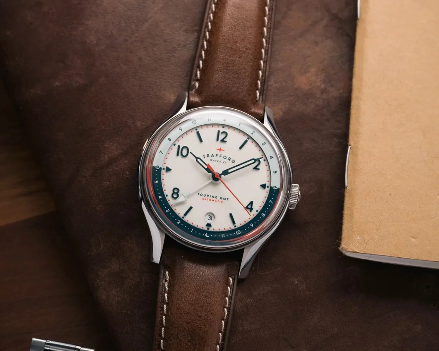 Silver round watch with white dial, black numerals, red second hand, and brown leather strap on a brown surface.