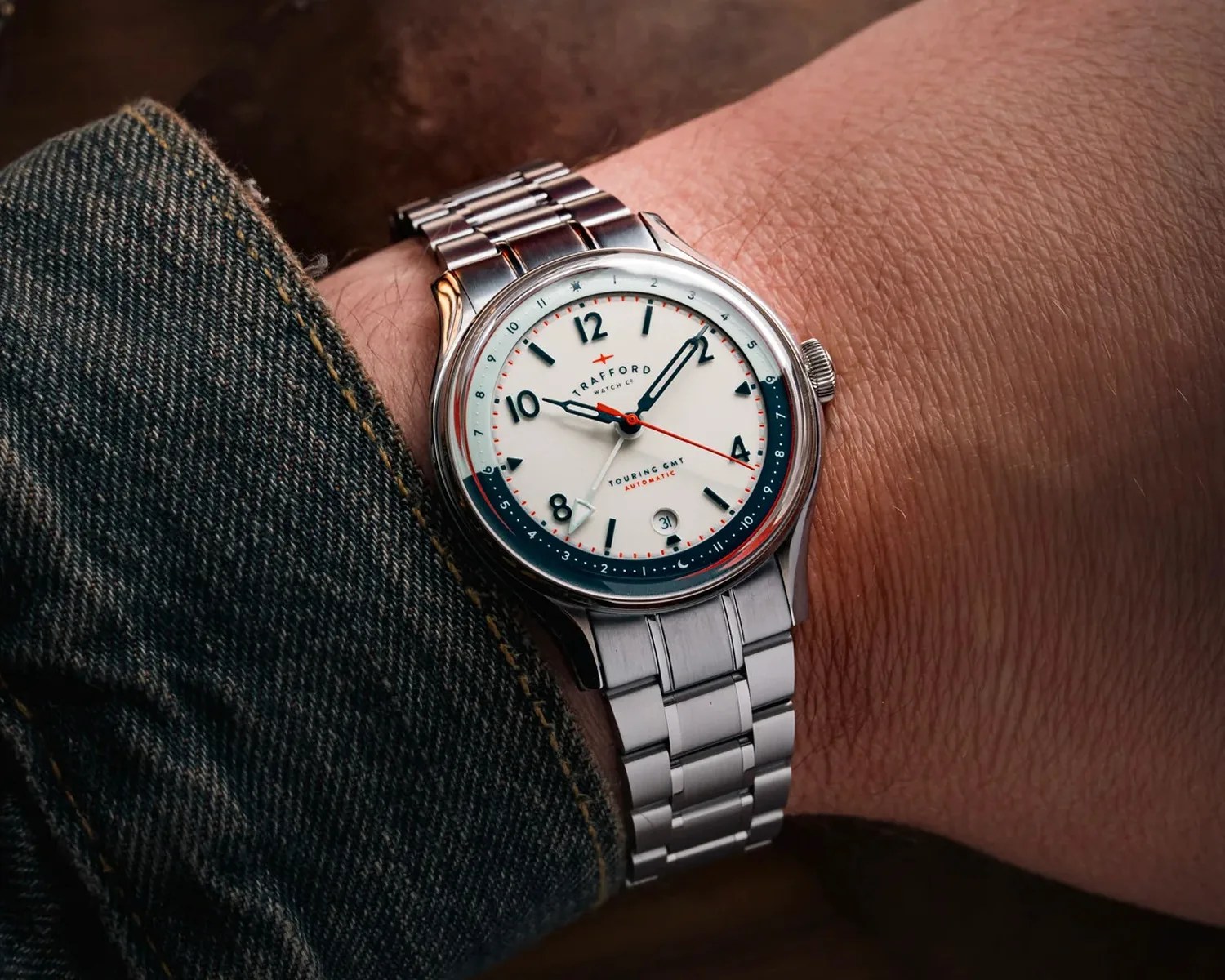 Silver metal wristwatch with white dial, black numerals, red second hand, and blue GMT ring worn on wrist.