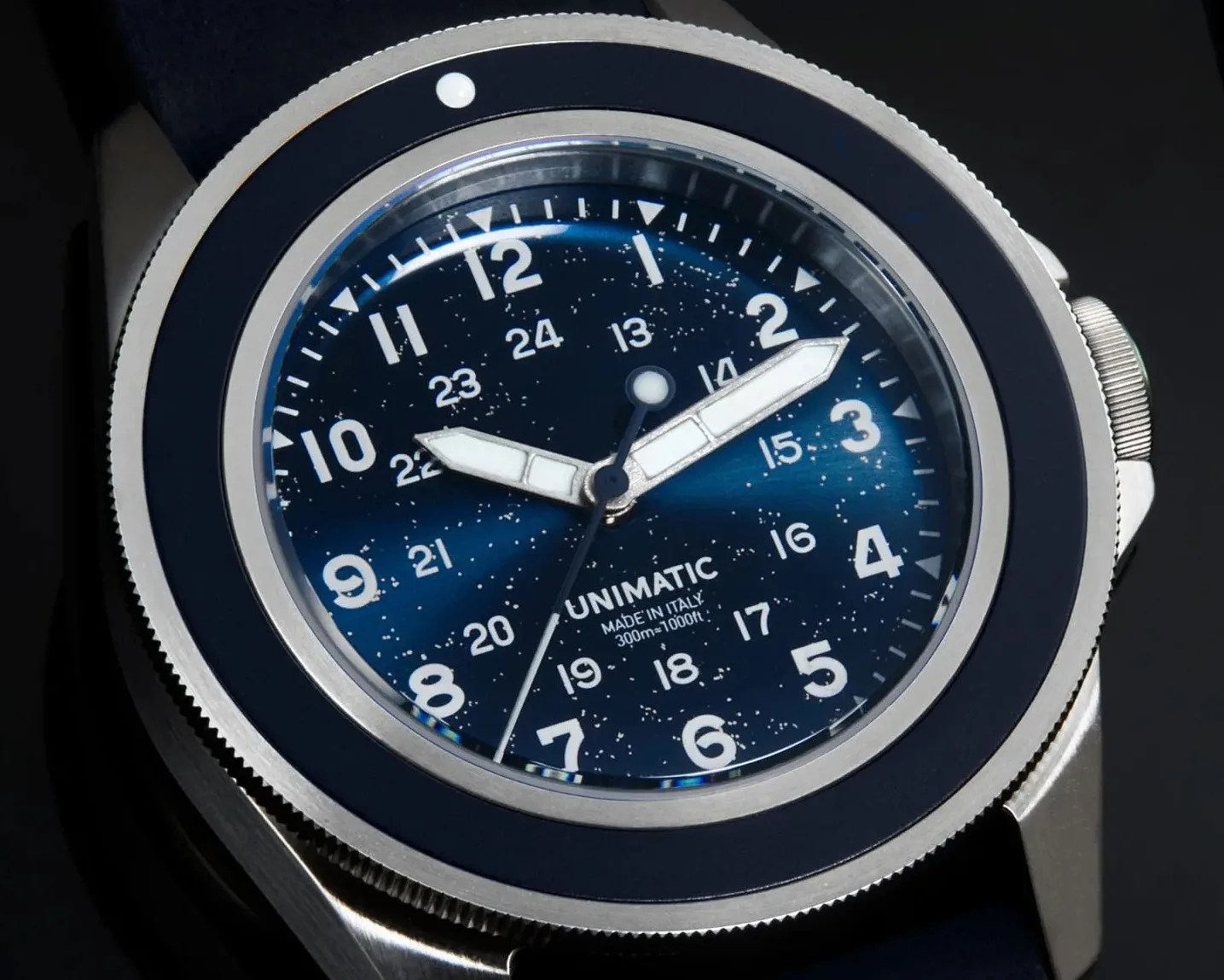 Close-up of a Unimatic wristwatch with a blue speckled dial, white hour markers, and luminous hands.