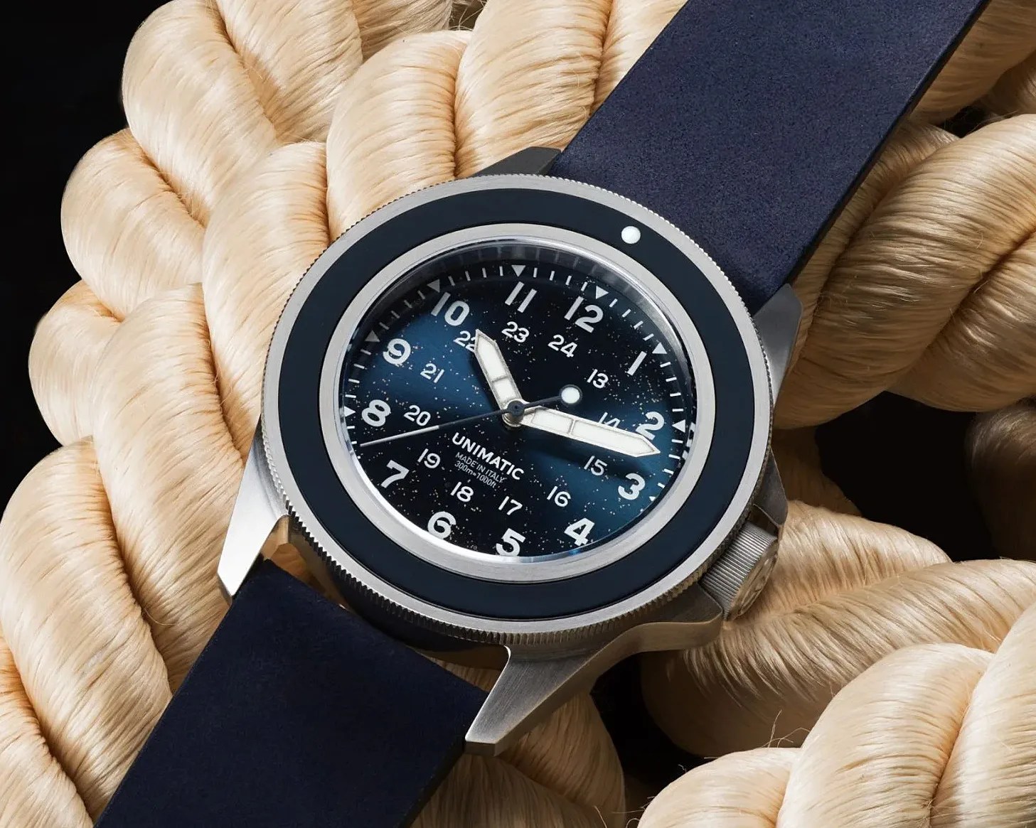 Stainless steel Unimatic wristwatch with a blue starry dial and black bezel on a dark blue strap, resting on thick beige rope.