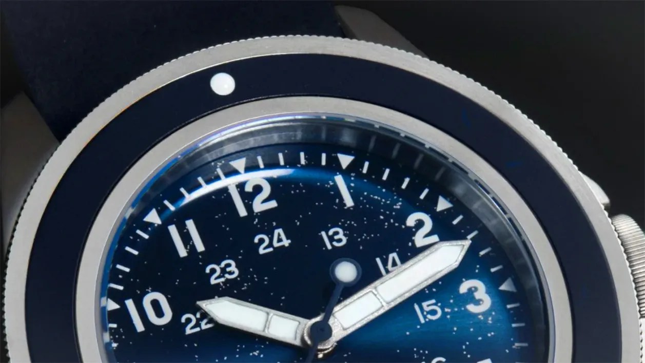 Close-up of a blue watch face with white hour and minute hands, white numerals, and a silver bezel.