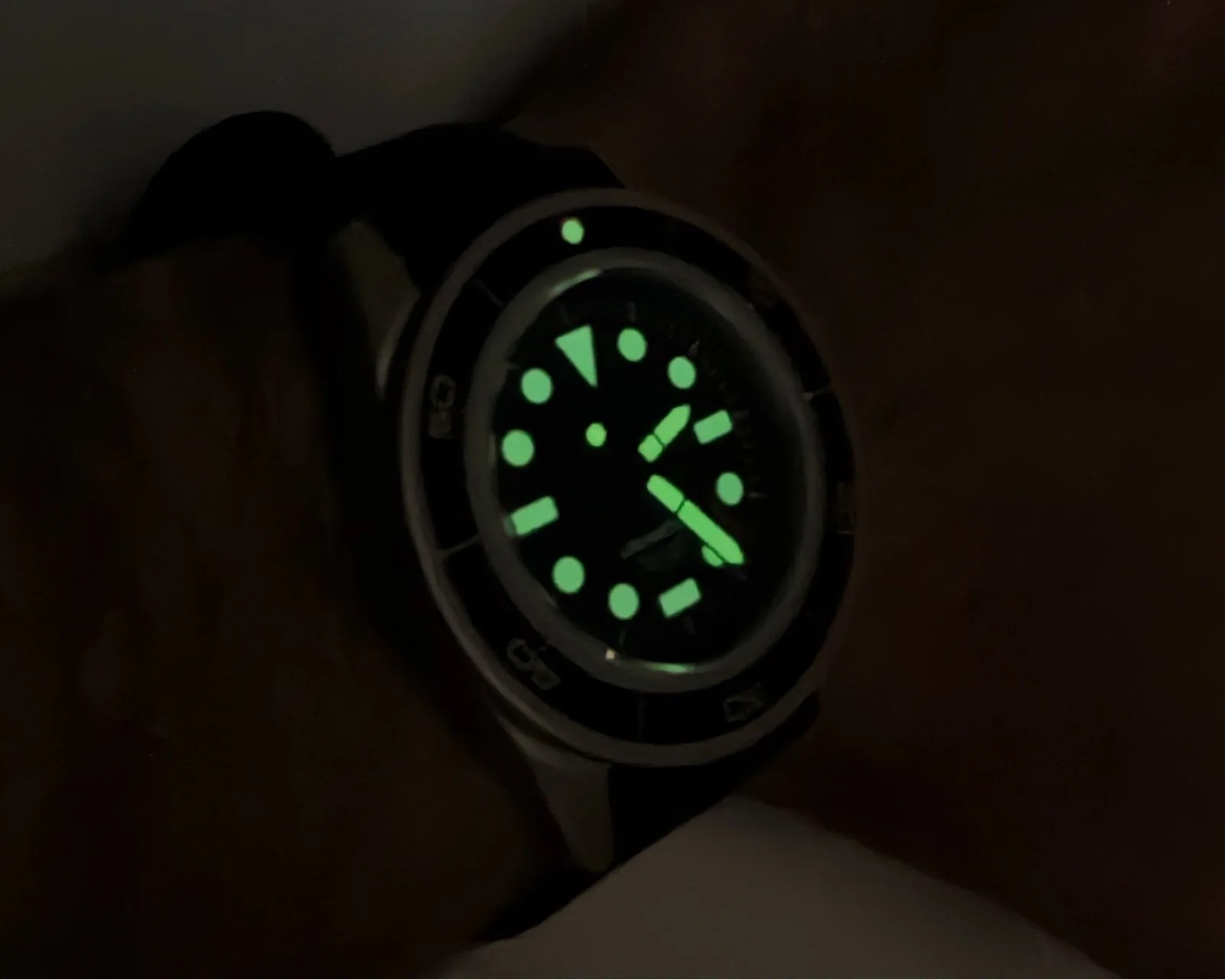 Wristwatch with glowing green hour markers and hands in a dark setting.