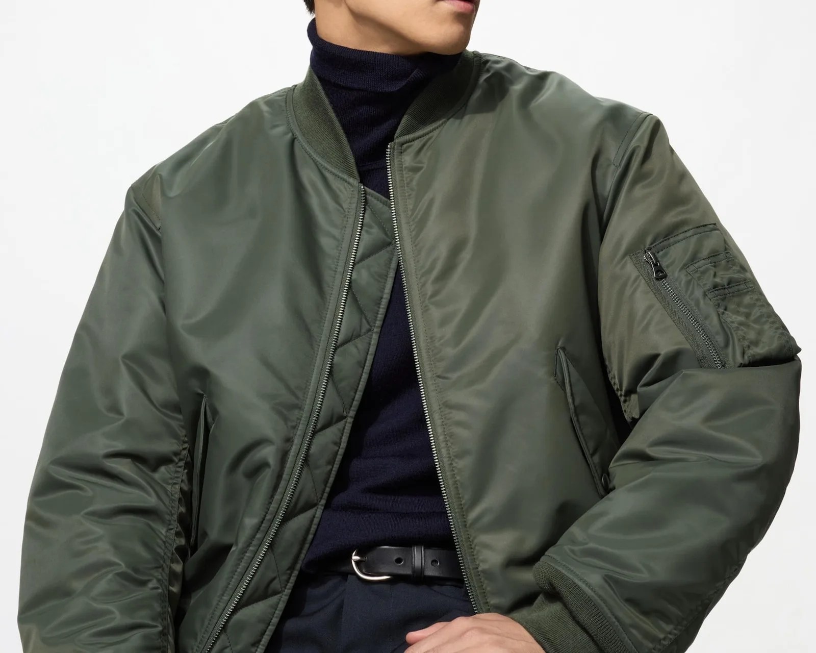 Olive green bomber jacket with zippered sleeve pocket worn over a navy turtleneck sweater.