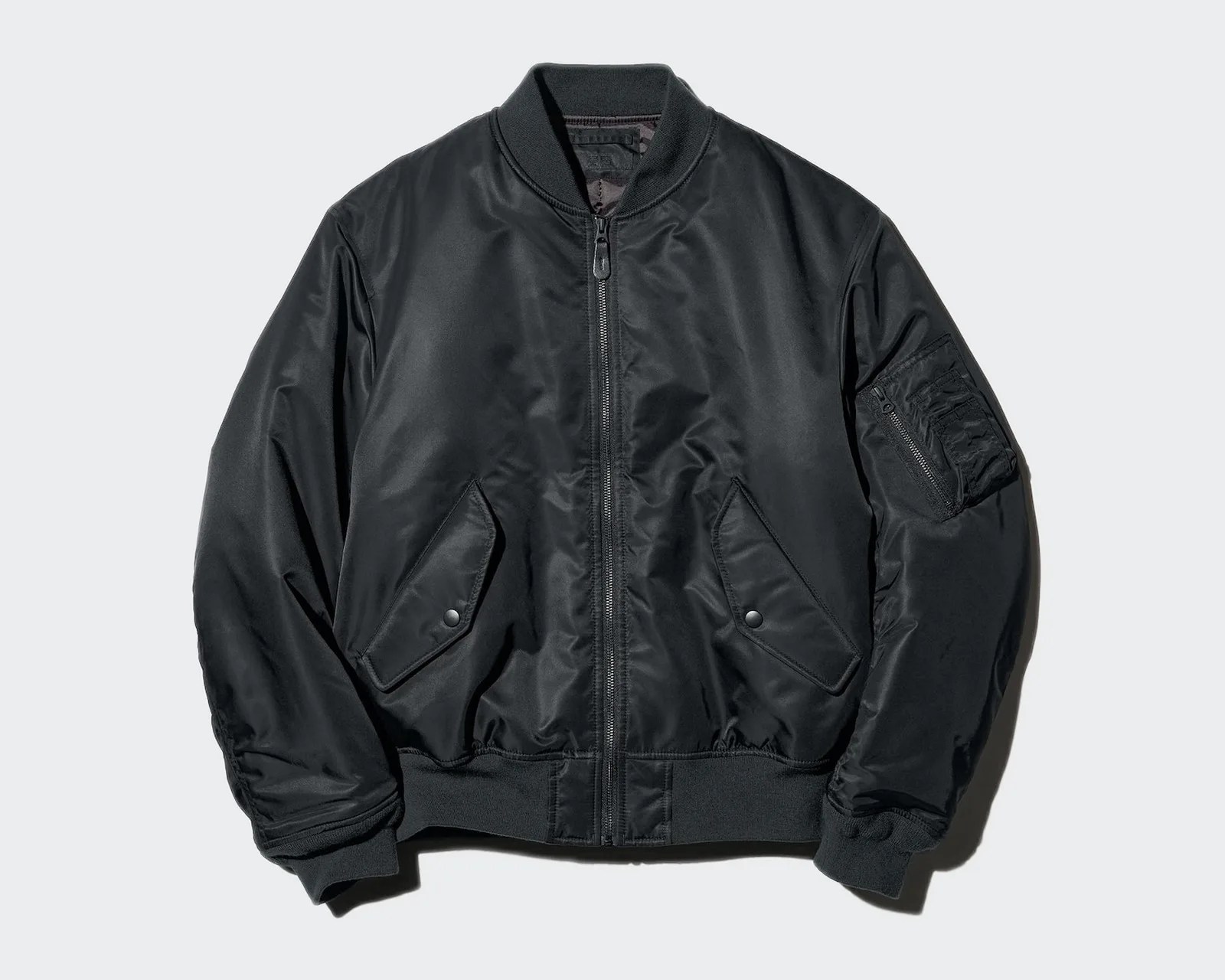Black bomber jacket with front zipper, two snap-button flap pockets, ribbed cuffs, and a zippered pocket on the left sleeve.
