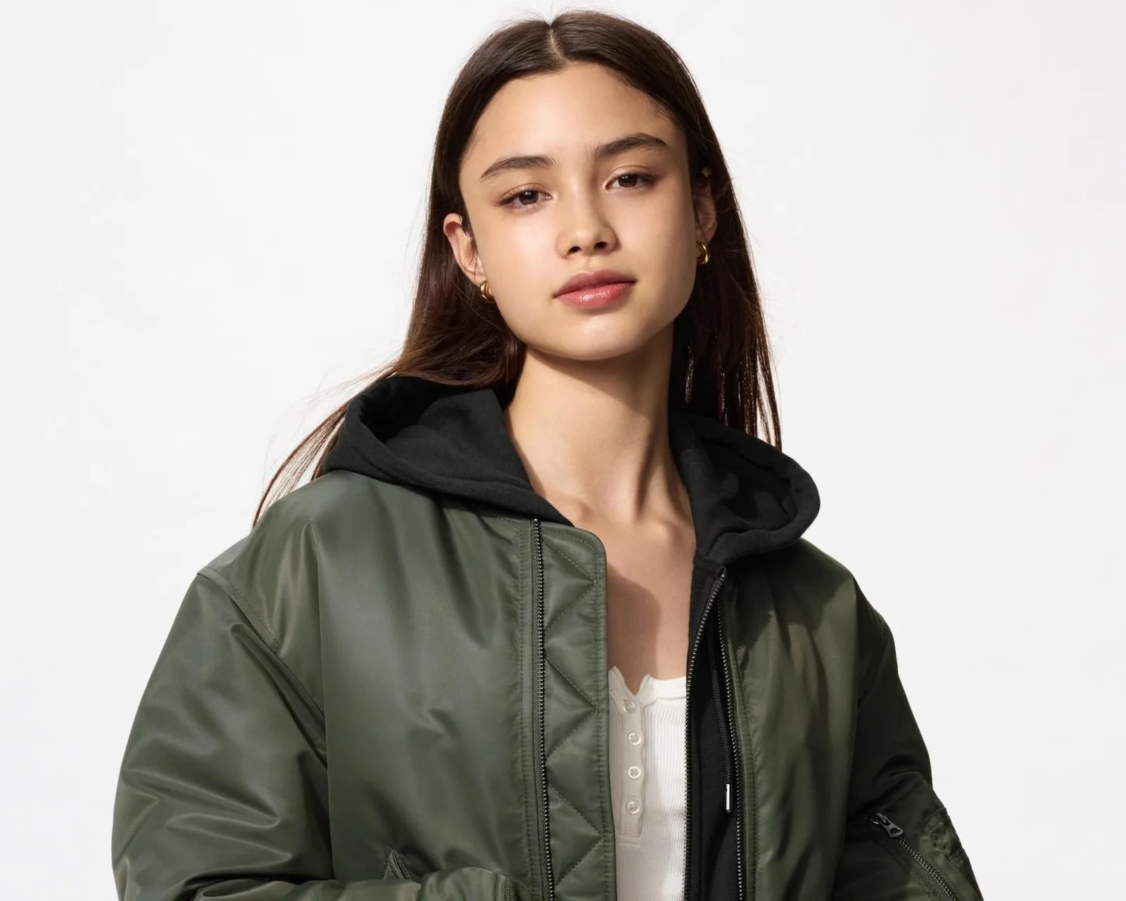 Young woman wearing a dark green bomber jacket over a black hoodie and white buttoned shirt.