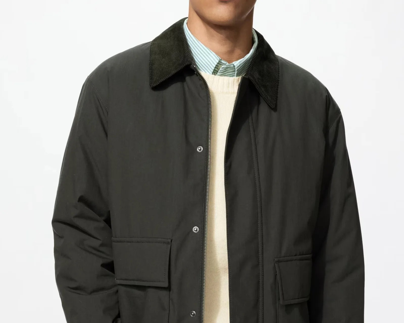 Black zip-up jacket with corduroy collar and flap pockets worn over a cream sweater and green striped shirt.