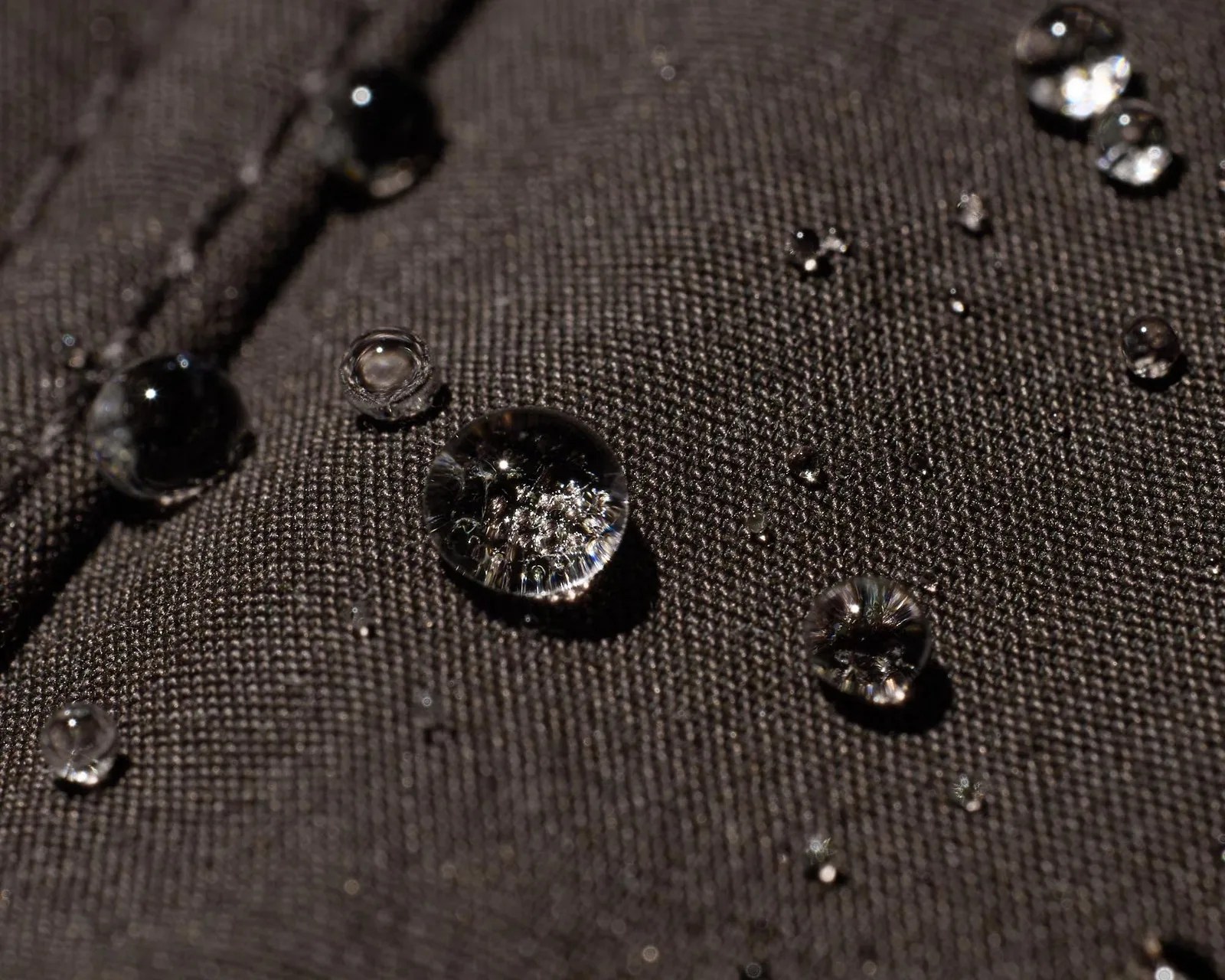 Clear water droplets beading on dark textured fabric.