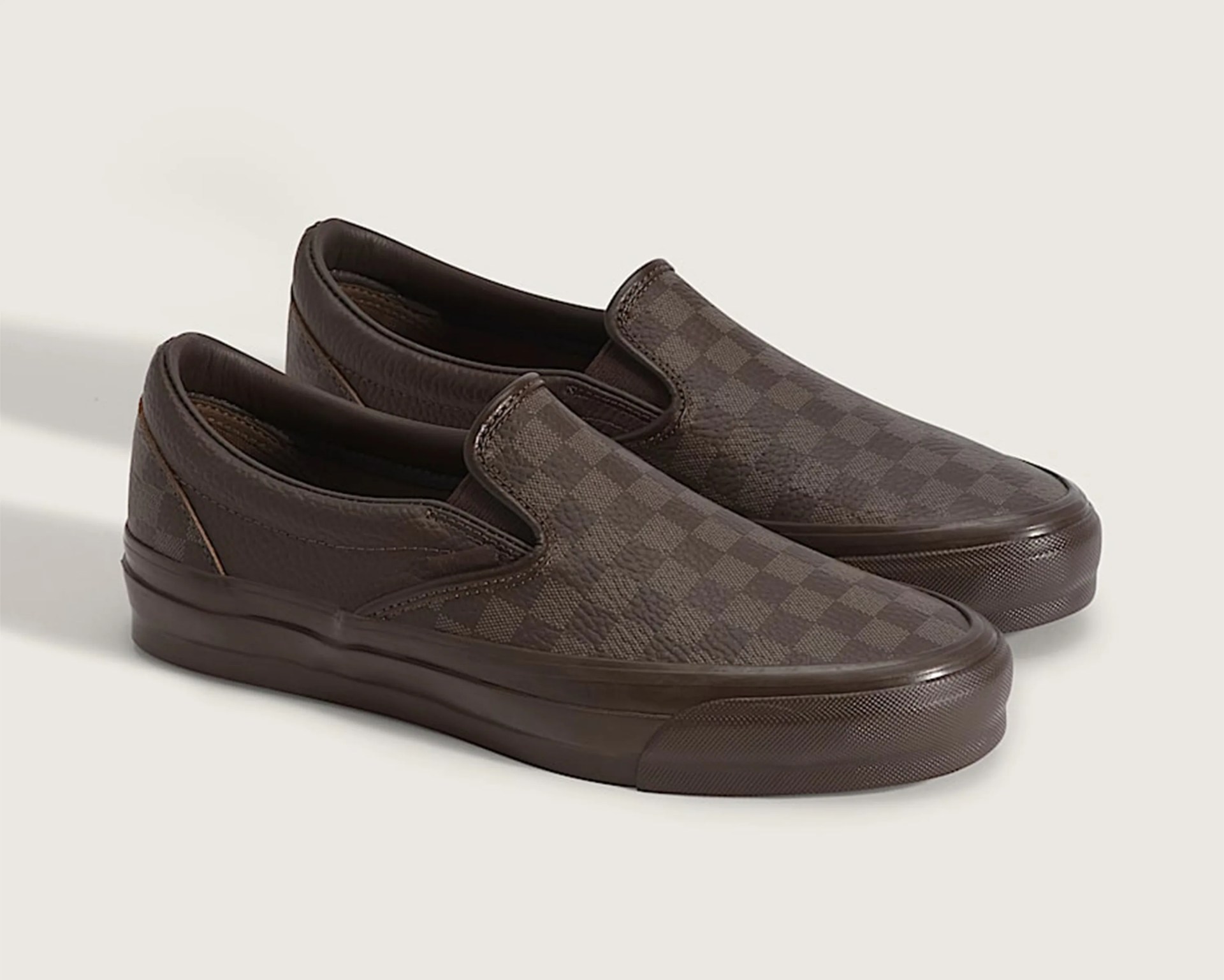 Pair of brown slip-on shoes with checkered pattern and rubber soles on a light background.