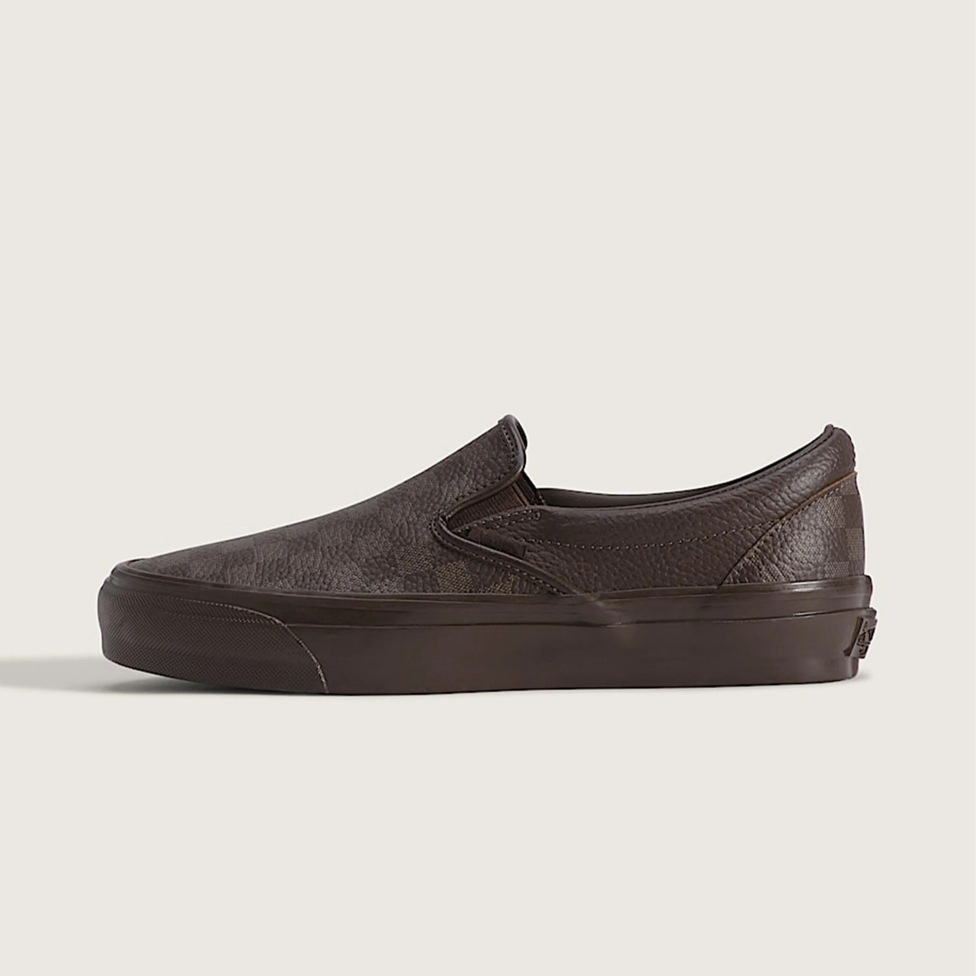Dark brown leather slip-on sneaker with textured finish and rubber sole on a beige background.