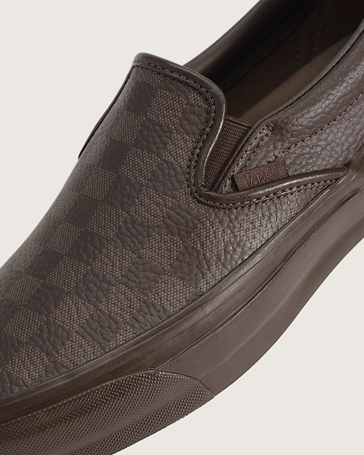 Dark brown leather slip-on shoe with checkerboard pattern and Vans logo tag on side.