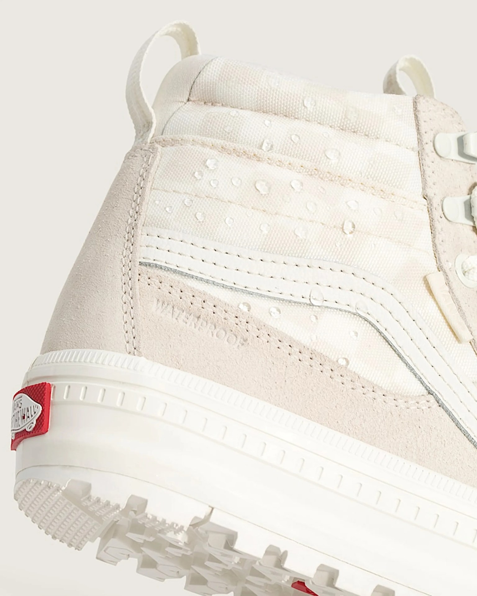 Close-up of a beige waterproof sneaker with water droplets on the fabric and a white sole with a red Vans logo tab.