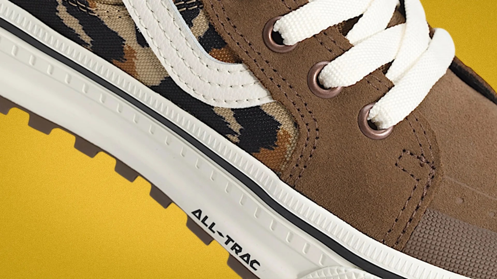 Close-up of a brown suede and camouflage canvas sneaker with white laces and a white sole labeled "ALL-TRAC.