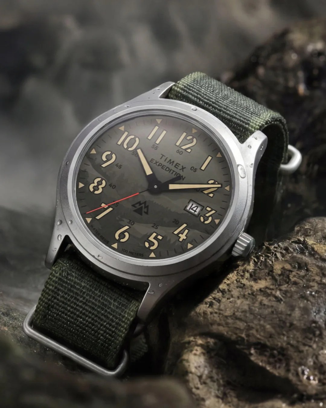 Timex Expedition wristwatch with green fabric strap and water droplets on a rocky surface.