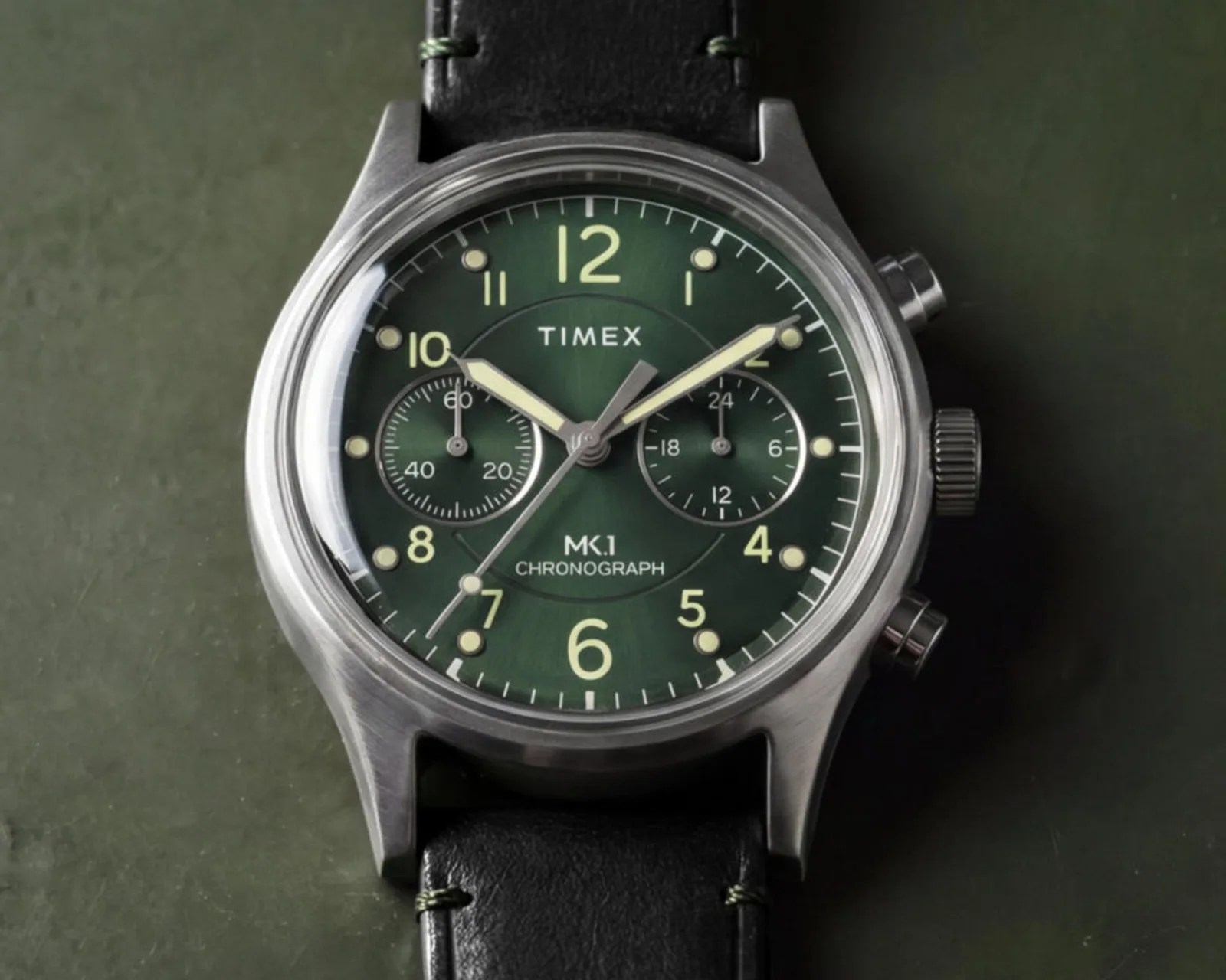 Timex MK1 chronograph watch with green dial, luminous hands, stainless steel case, and black leather strap.