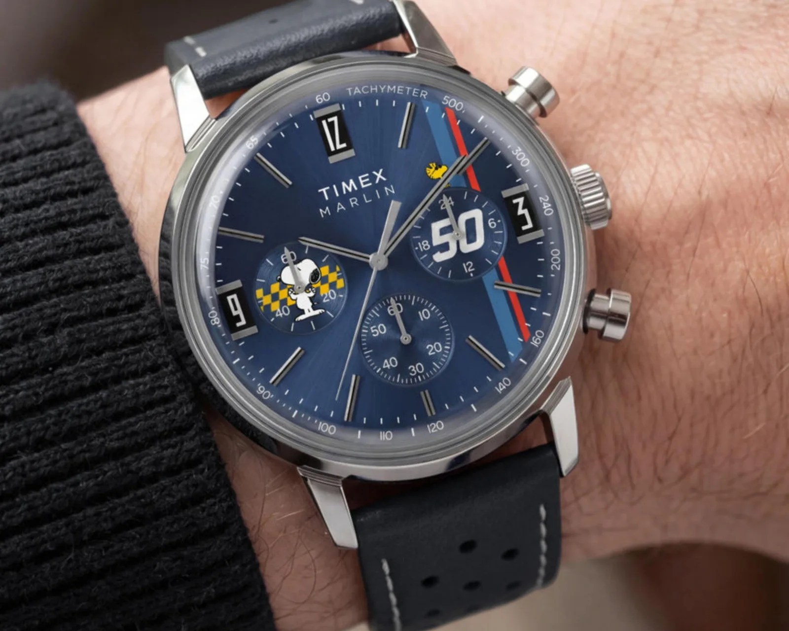 Blue Timex Marlin wristwatch with Snoopy and Woodstock illustrations, tachymeter scale, and black leather strap worn on a wrist.