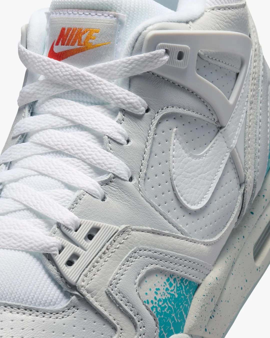 Close-up of a white Nike sneaker with white laces, a white leather upper, and teal speckled midsole detailing.
