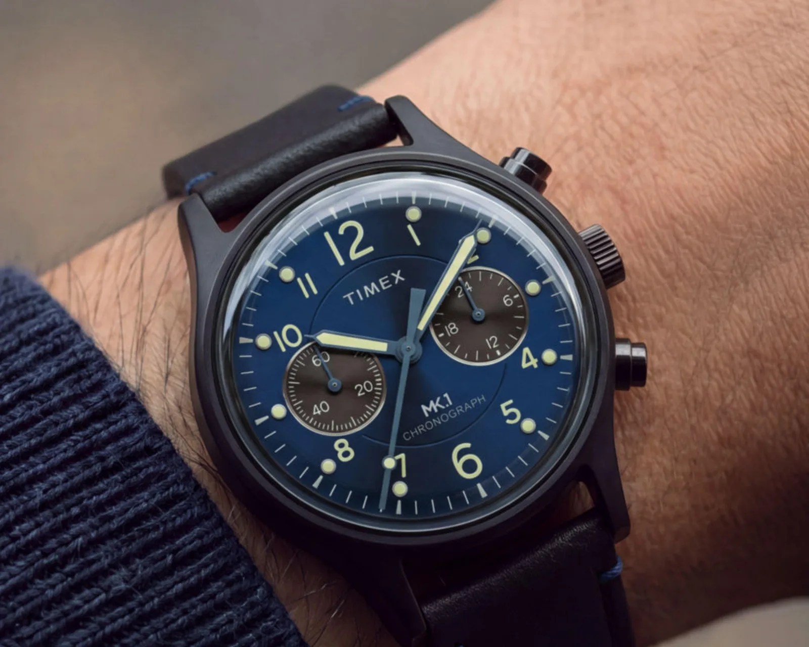 Black Timex MK1 chronograph watch with blue dial and leather strap worn on a wrist.