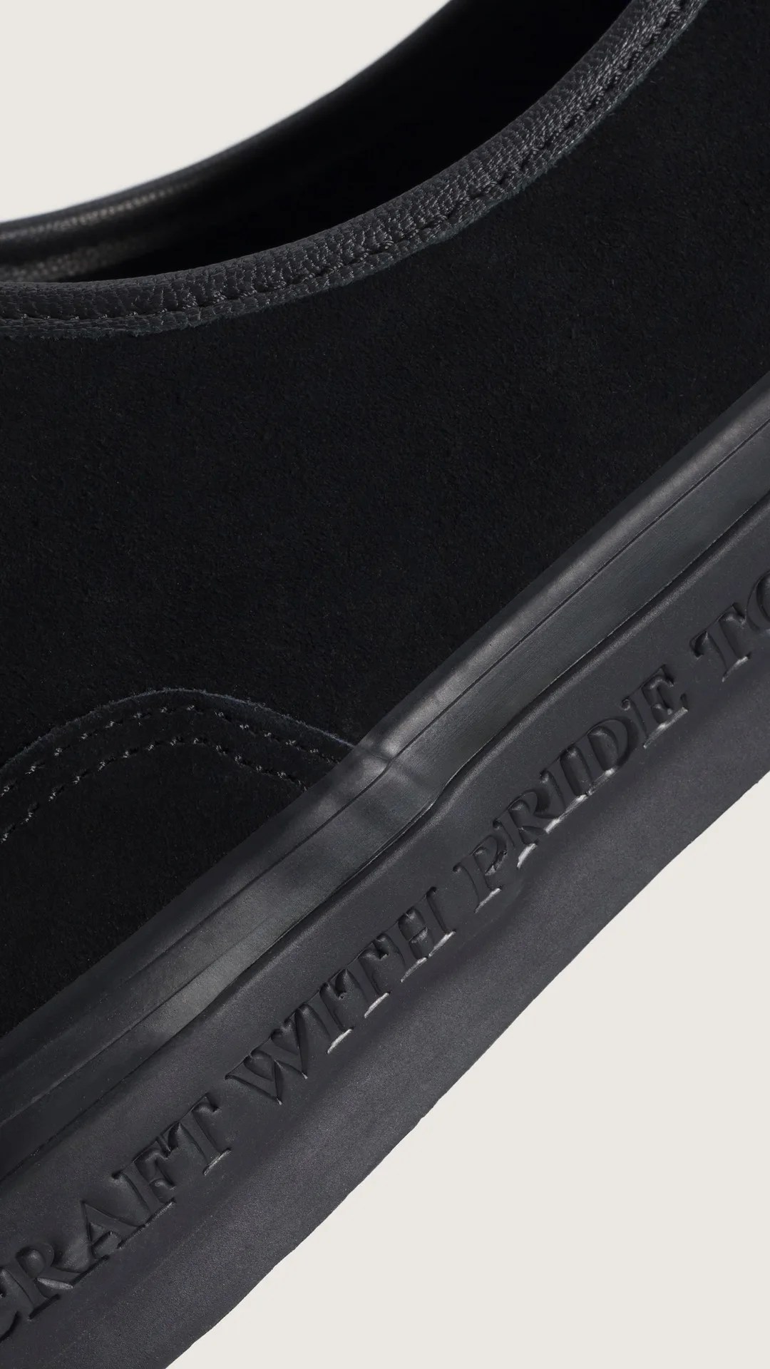 Close-up of a black suede shoe with black rubber sole embossed with partial text.