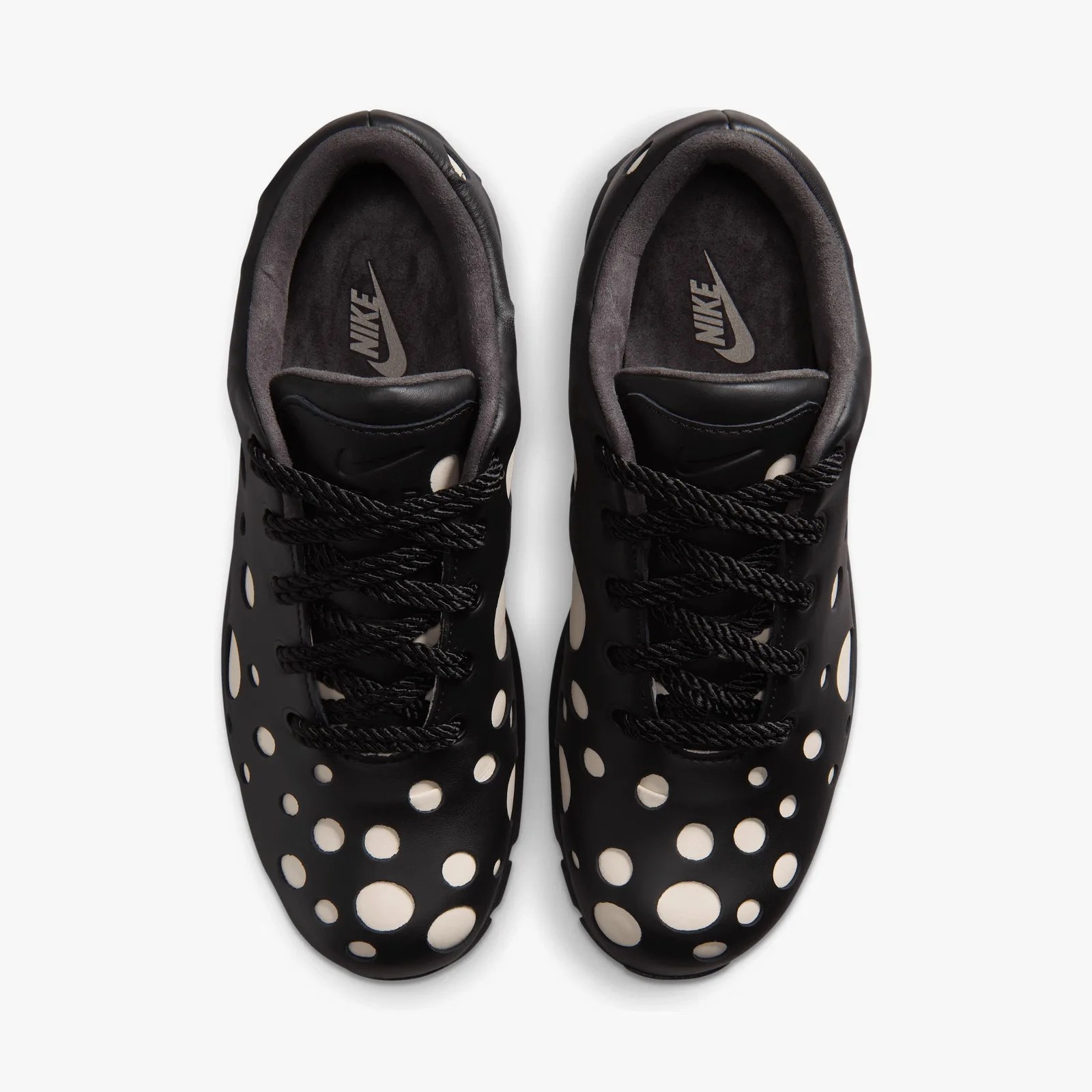 Top view of black Nike sneakers with white circular cutouts and black laces on a white background.