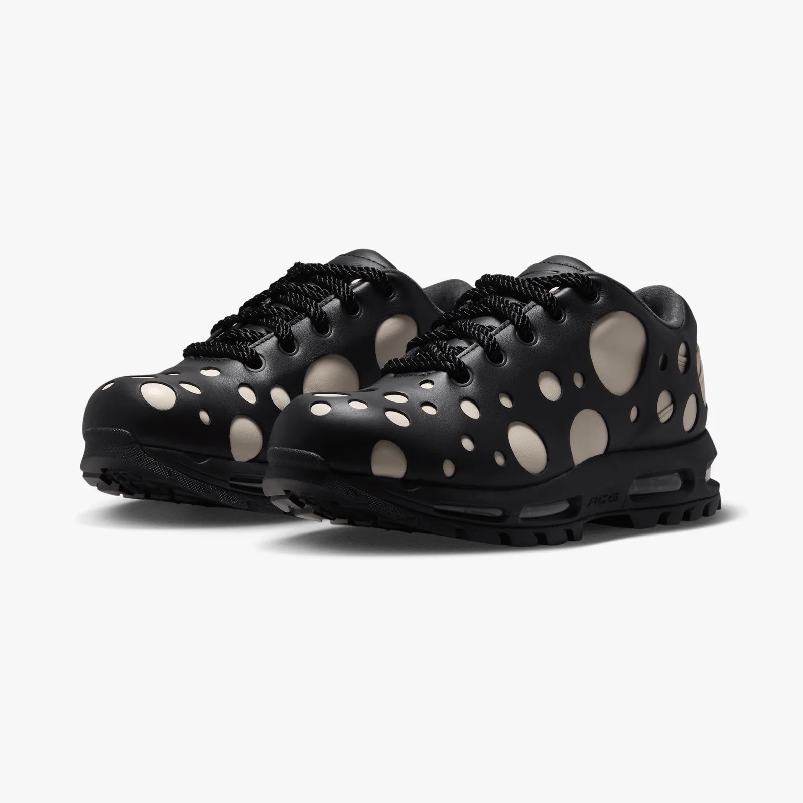 Black sneakers with large beige circular cutouts and thick black laces on a white background.