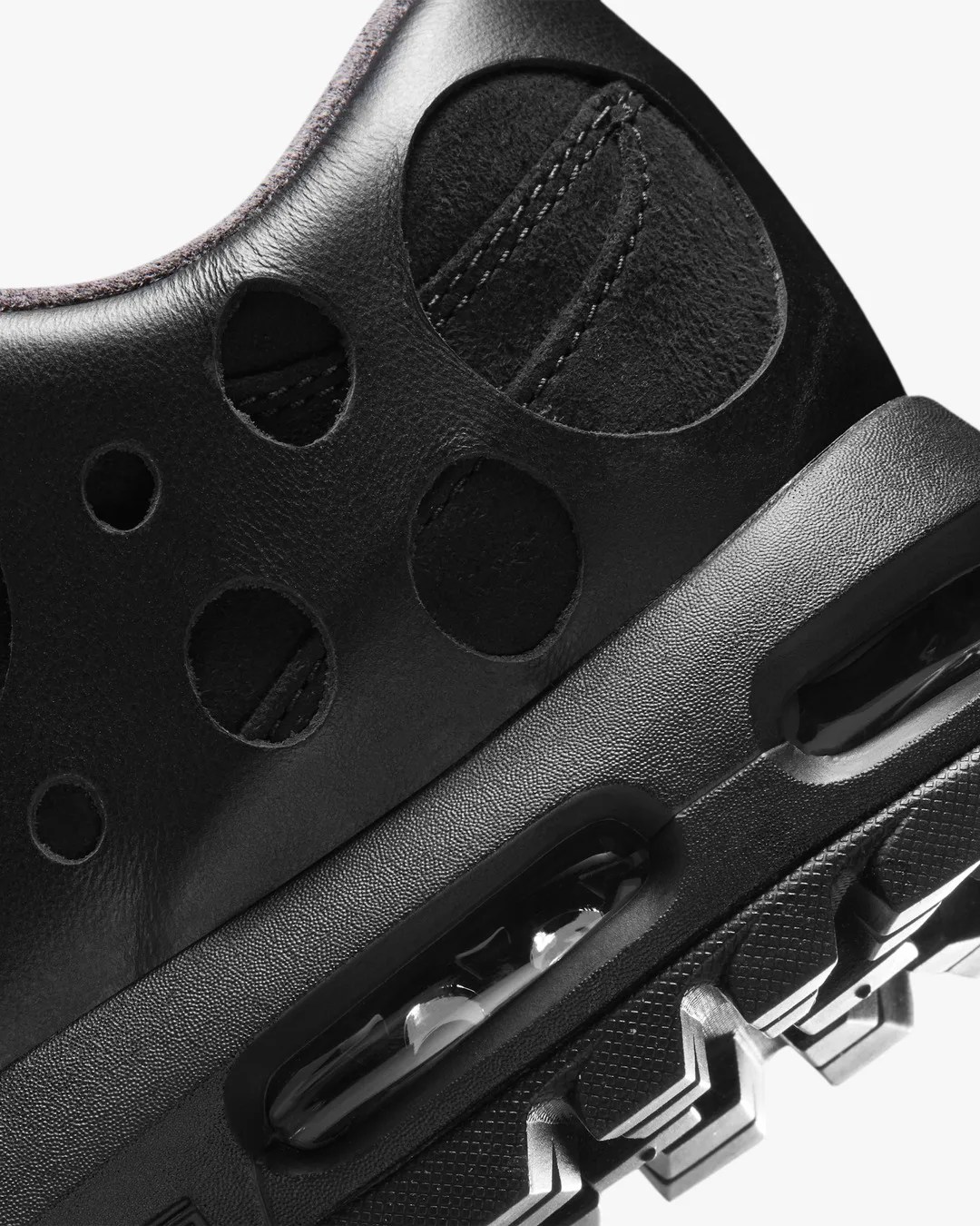 Close-up of black sneaker with circular cutouts on leather upper and visible air cushioning in the sole.