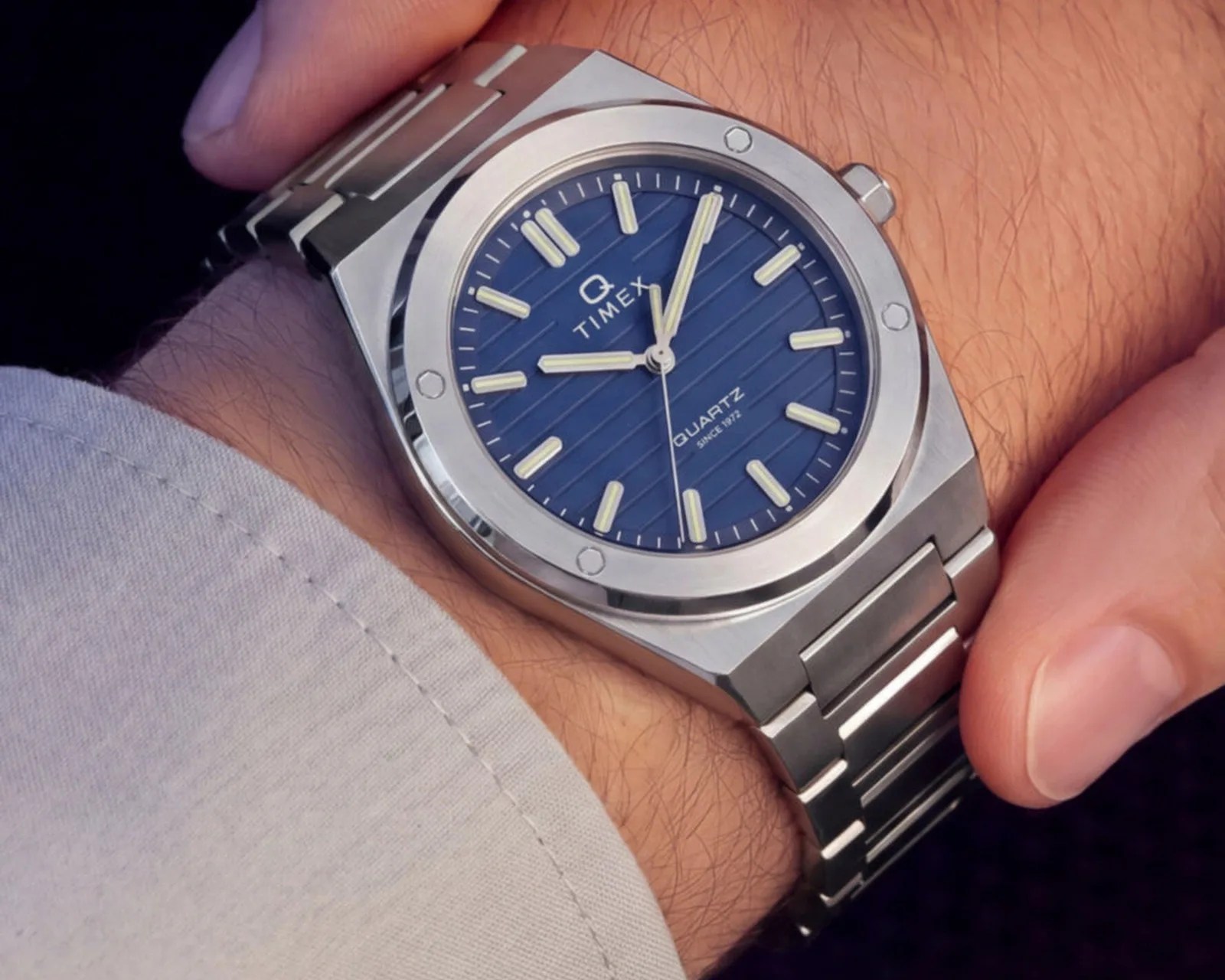 Silver Timex Q quartz wristwatch with a blue dial and luminous hour markers on a metal bracelet.