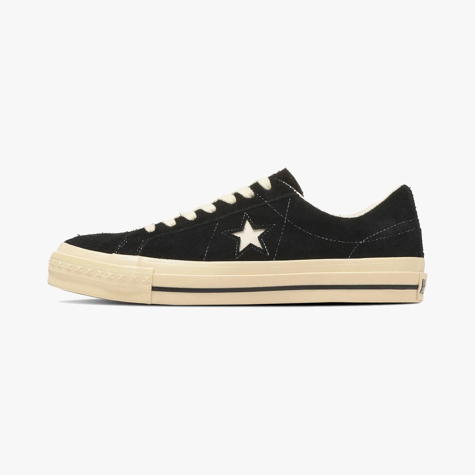 Black low-top sneaker with white star cutout and cream rubber sole with black stripe.
