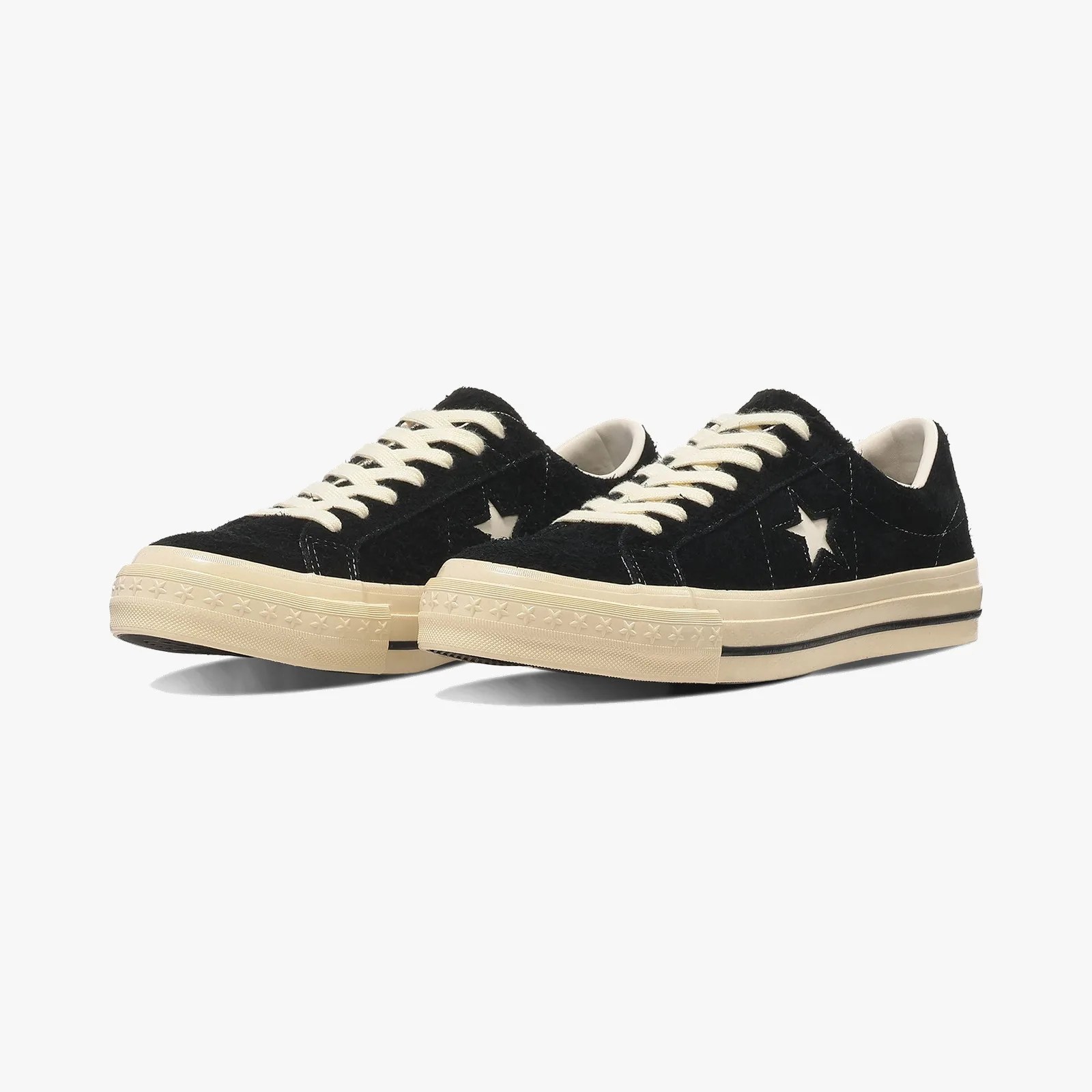 Pair of black low-top sneakers with white star logo, cream laces, and cream rubber soles with star pattern.
