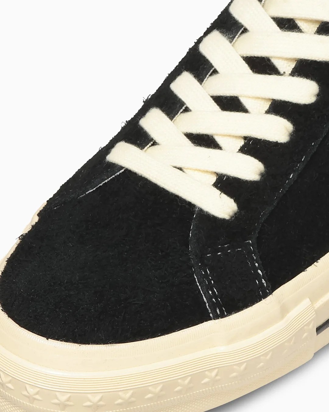 Close-up of a black suede sneaker with cream-colored laces and a cream rubber sole featuring star patterns.