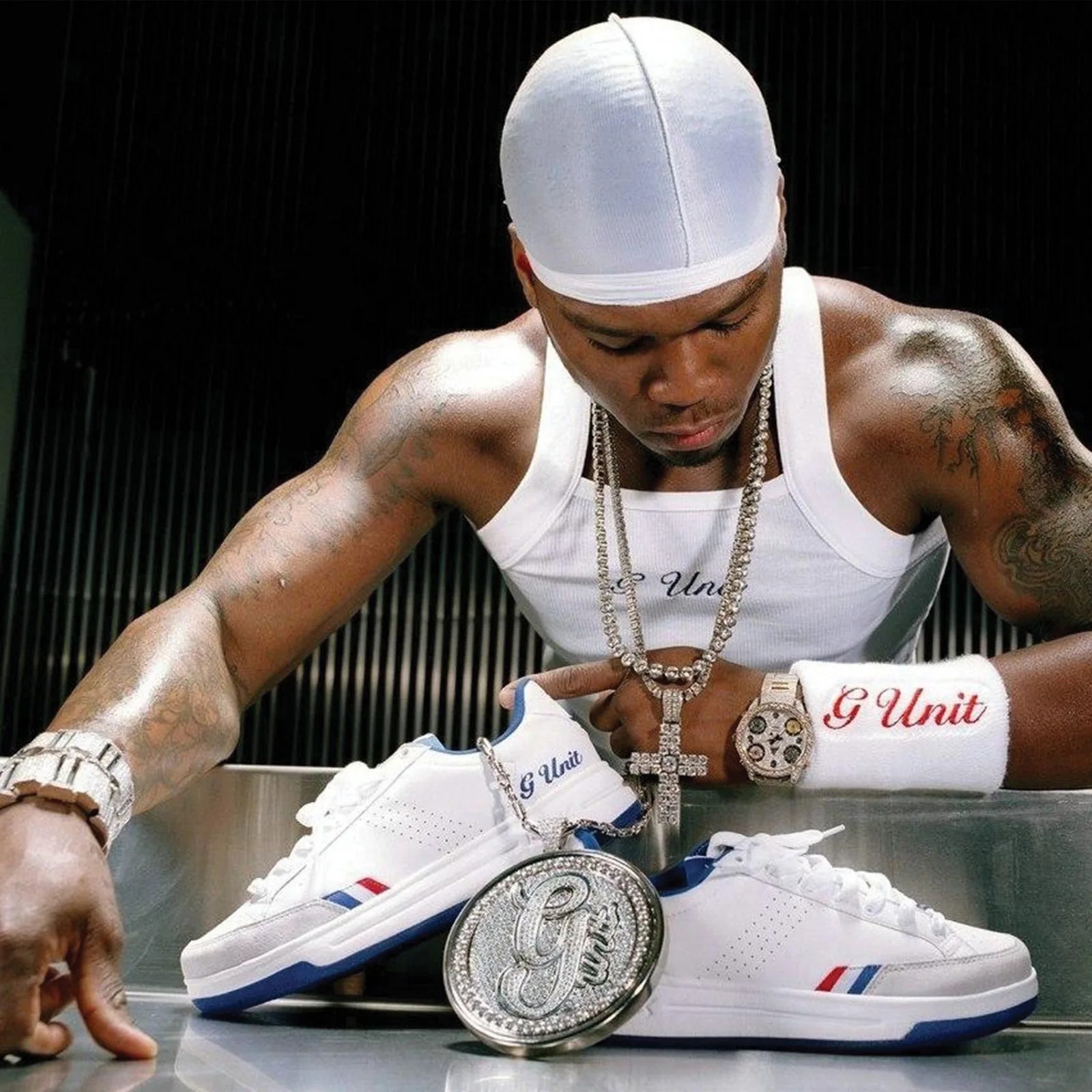 White sneakers with blue and red stripes and "G Unit" branding next to a large diamond-encrusted "G Unit" pendant.