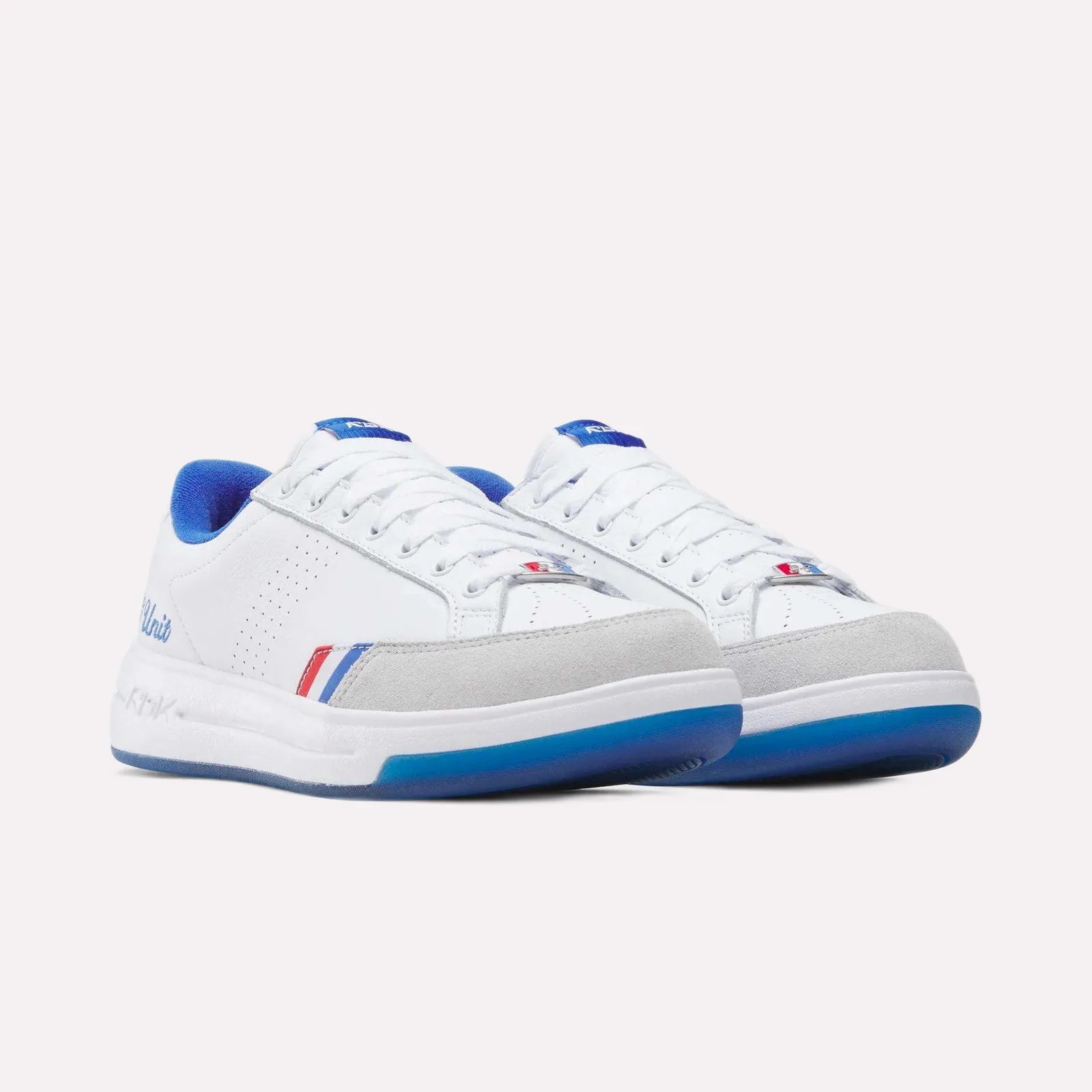 White low-top sneakers with blue inner lining, gray suede toe caps, and red, white, and blue stripe accents.