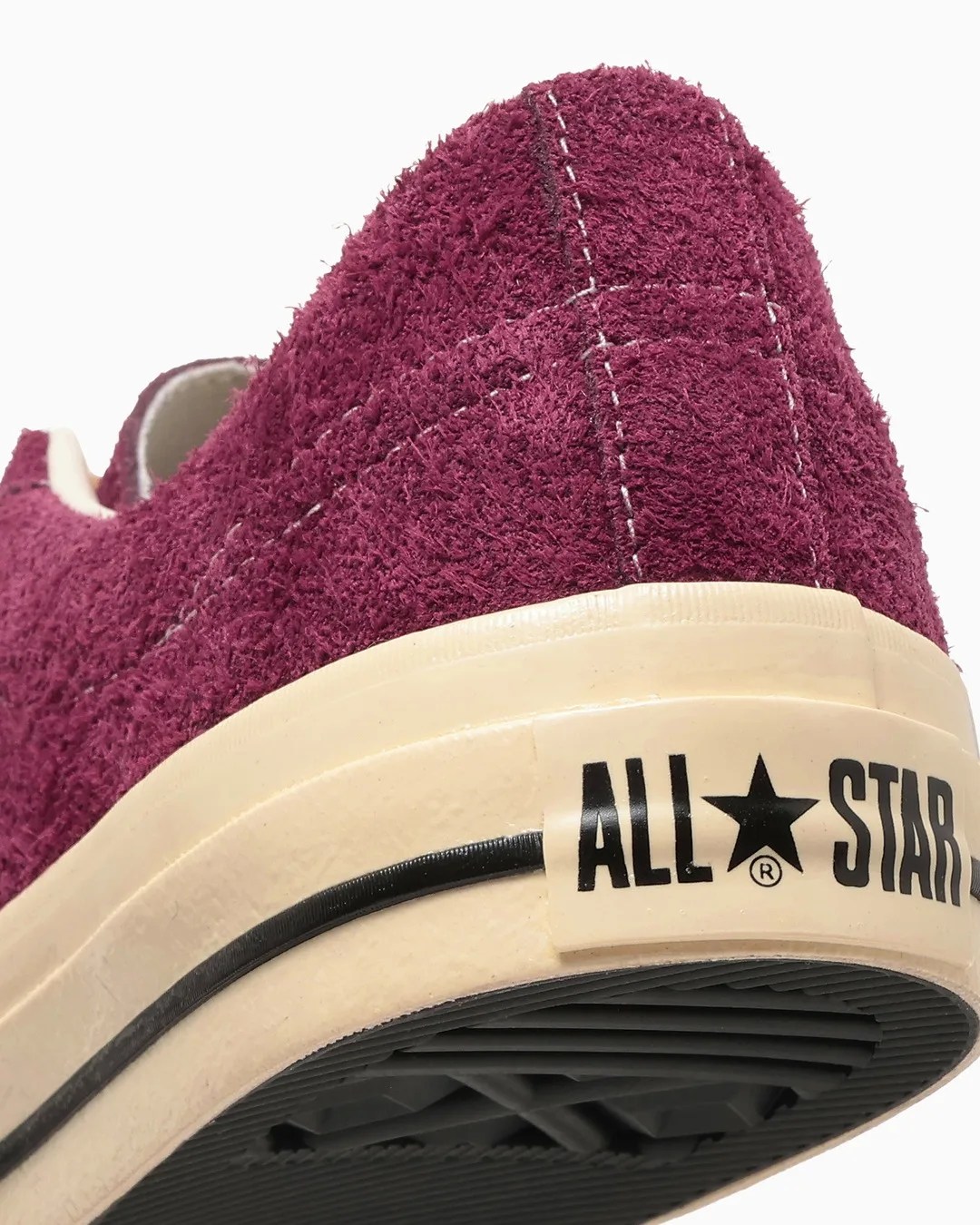 Close-up of the heel of a burgundy textured Converse All Star sneaker with a cream rubber sole and black stripe.