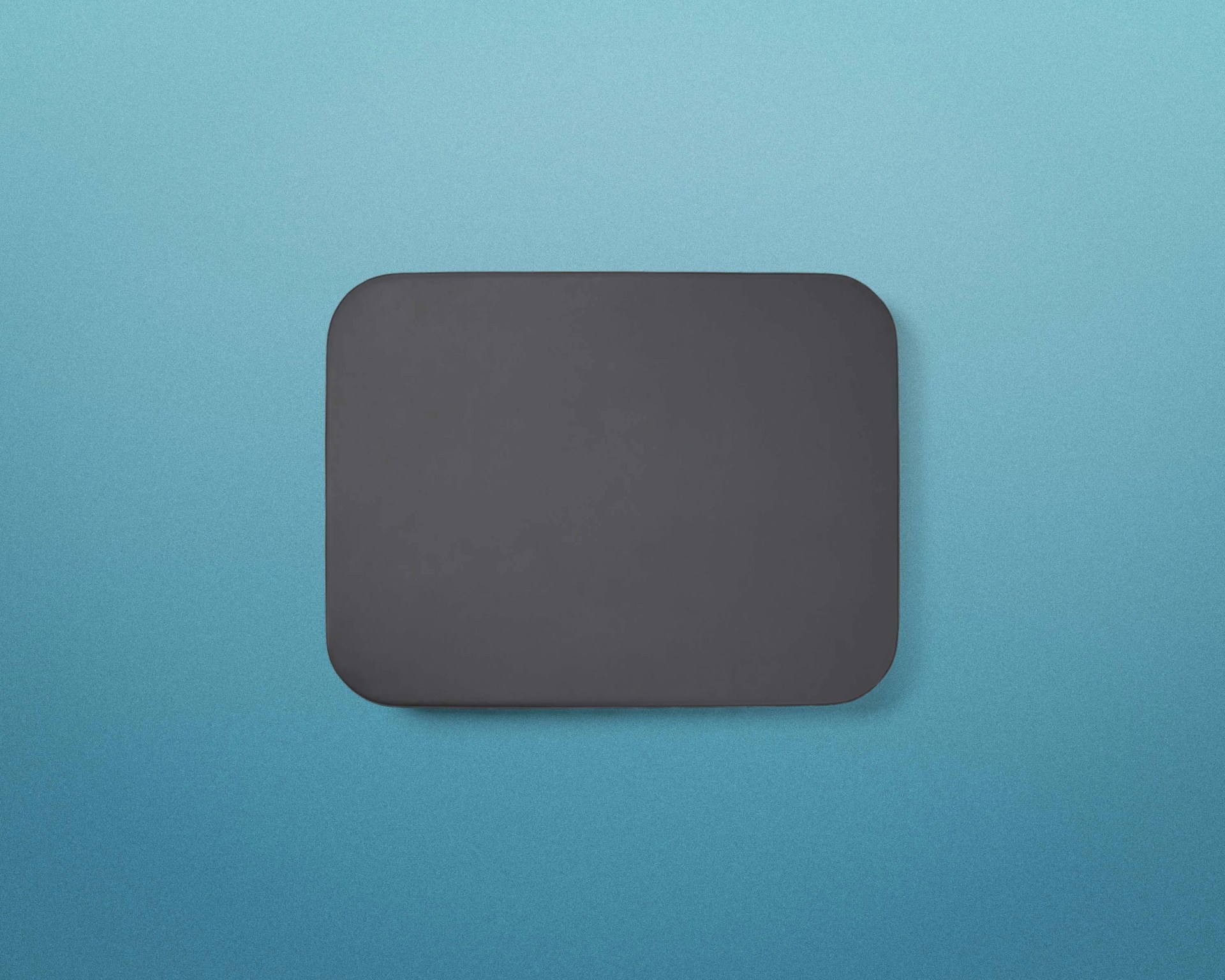 Dark gray rectangular object with rounded corners on a blue textured surface.
