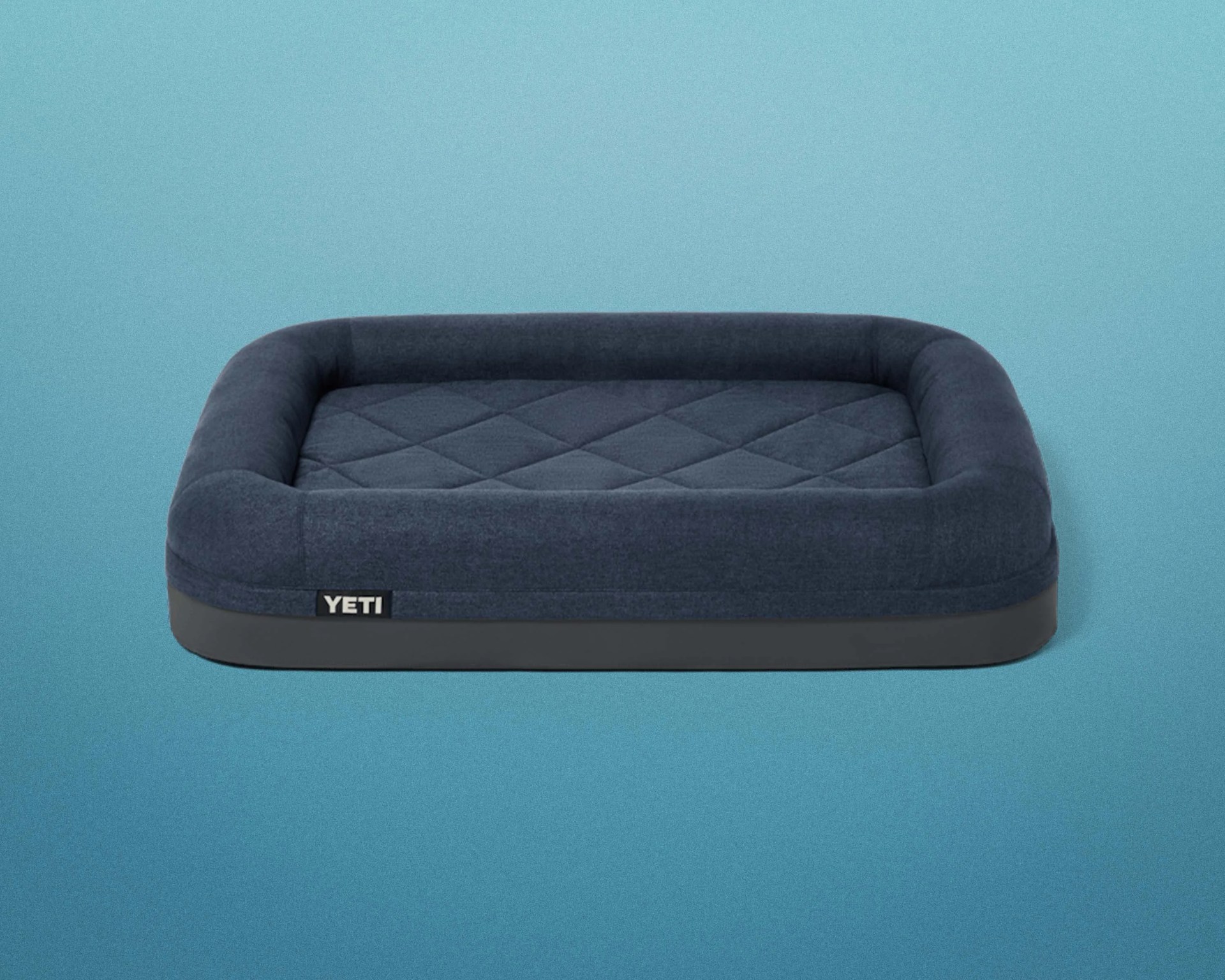 Dark blue rectangular dog bed with quilted cushion and raised sides on a blue background.
