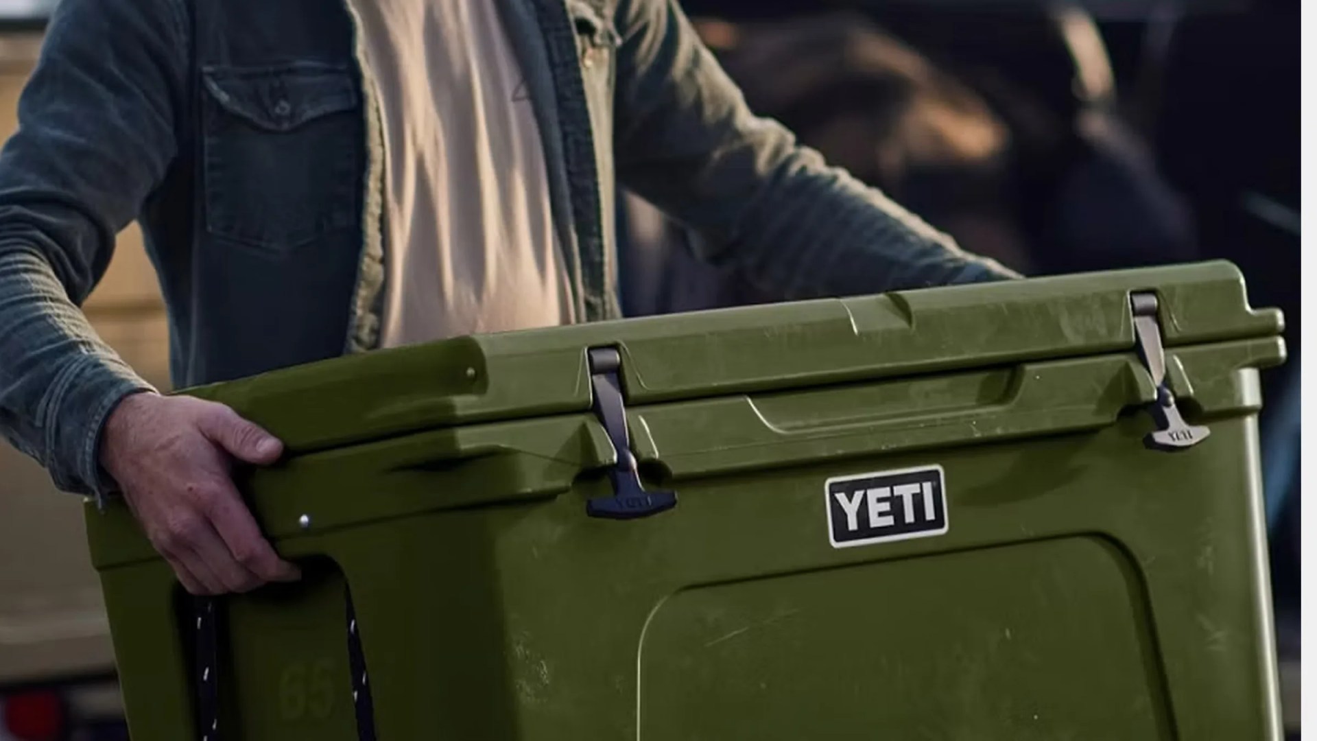 Olive green YETI cooler with black latches held by a person wearing a denim jacket.