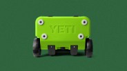 Bright green YETI cooler viewed from the bottom showing four white feet and two black wheels on a green background.